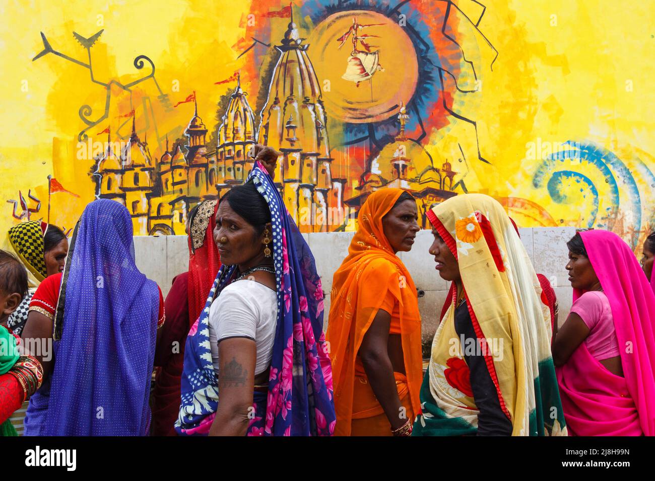 Orchha, Madhya Pradesh, India : un grupo de mujeres vestidas con saris coloridos recogen agua de una fuente en las afueras del templo Ram Raja. Mural que representa Chatu Foto de stock
