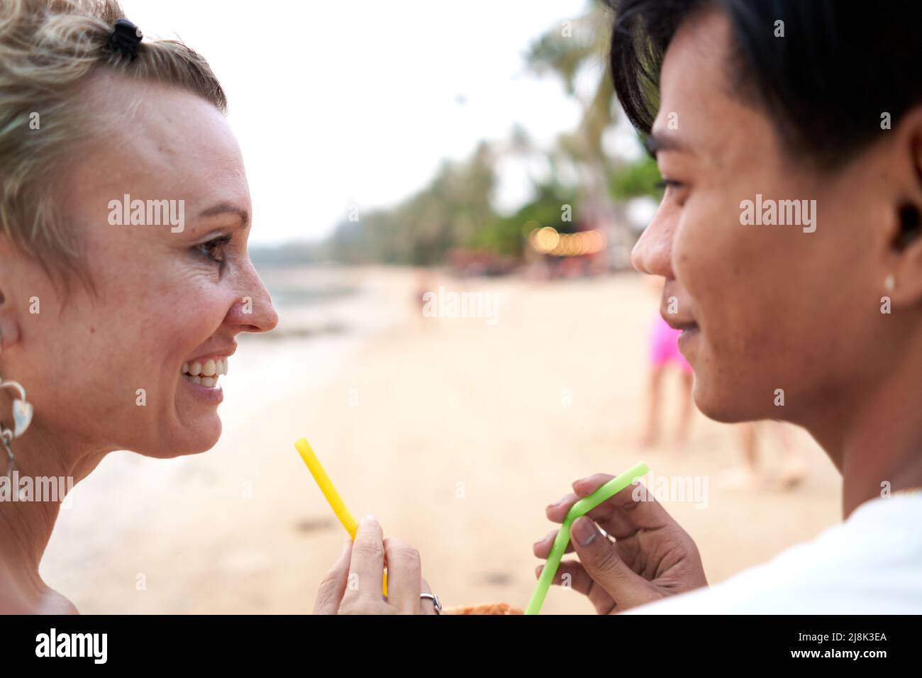 Los amantes se miran unos a otros mientras comparten un jugo de coco en la playa Foto de stock