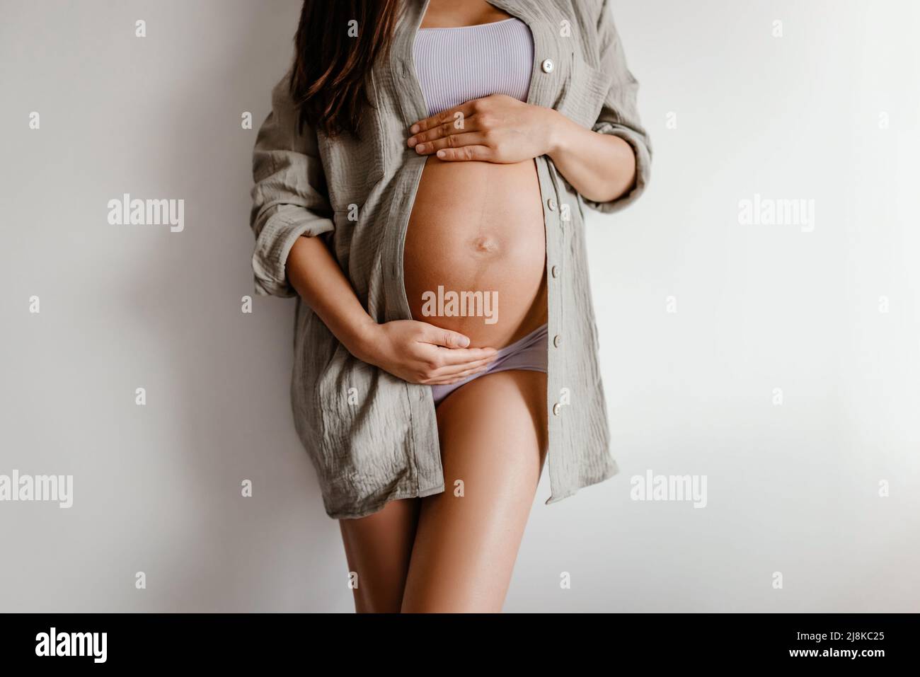 Primer plano del vientre durante el embarazo. Mujer embarazada con ropa interior y camisa de algodón informal en casa relajante holding esperando vientre para el cuidado de la piel, la salud Foto de stock