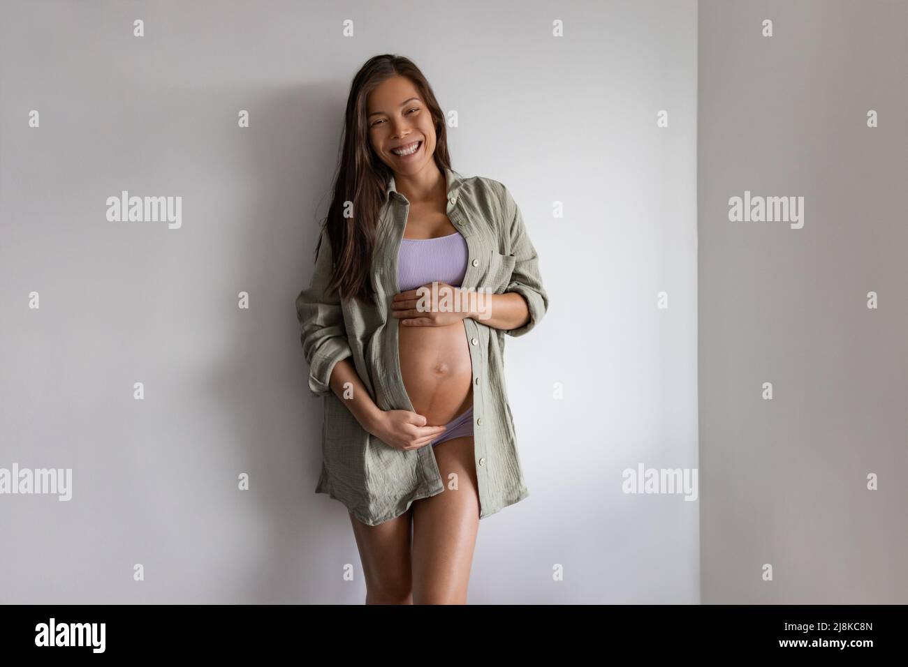 Retrato de una mujer embarazada asiática feliz en casa. Ropa interior de maternidad de embarazo, modelo que lleva ropa de algodón orgánico, camisa suelta y ropa de undies para Foto de stock