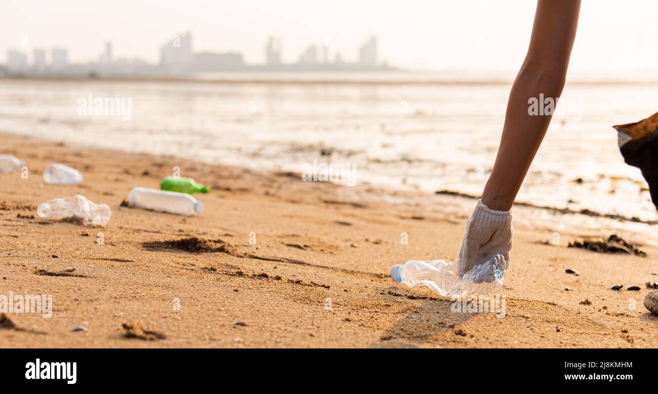 Mujer voluntaria recogiendo una botella de plástico en una bolsa plástico negro para limpiar la playa, la basura de limpieza femenina, el concepto de ecología y el mundo de Environ Fotografía