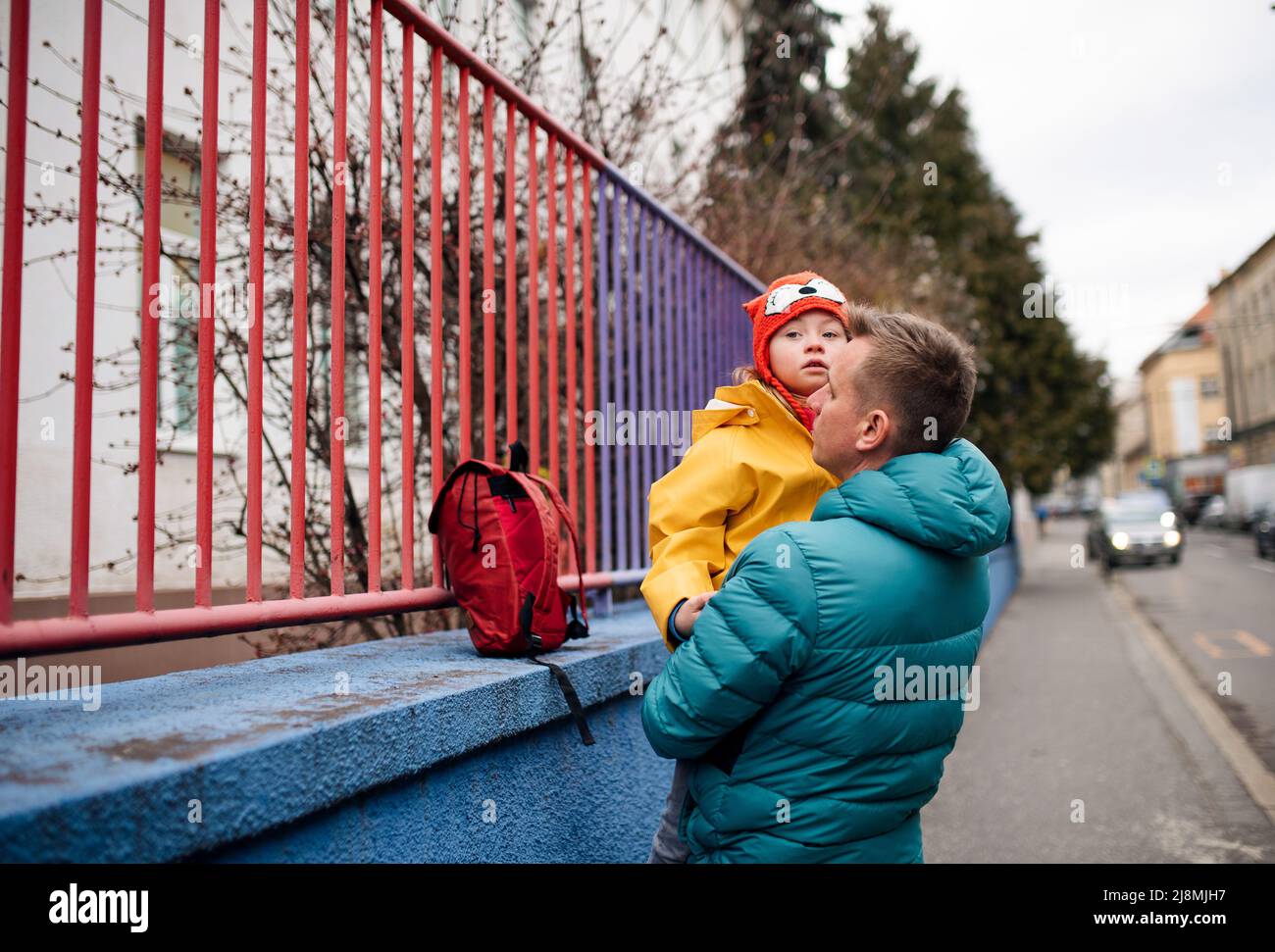 Padre llevando a su hija pequeña con síndrome de Down a la escuela, al aire libre en la calle. Foto de stock