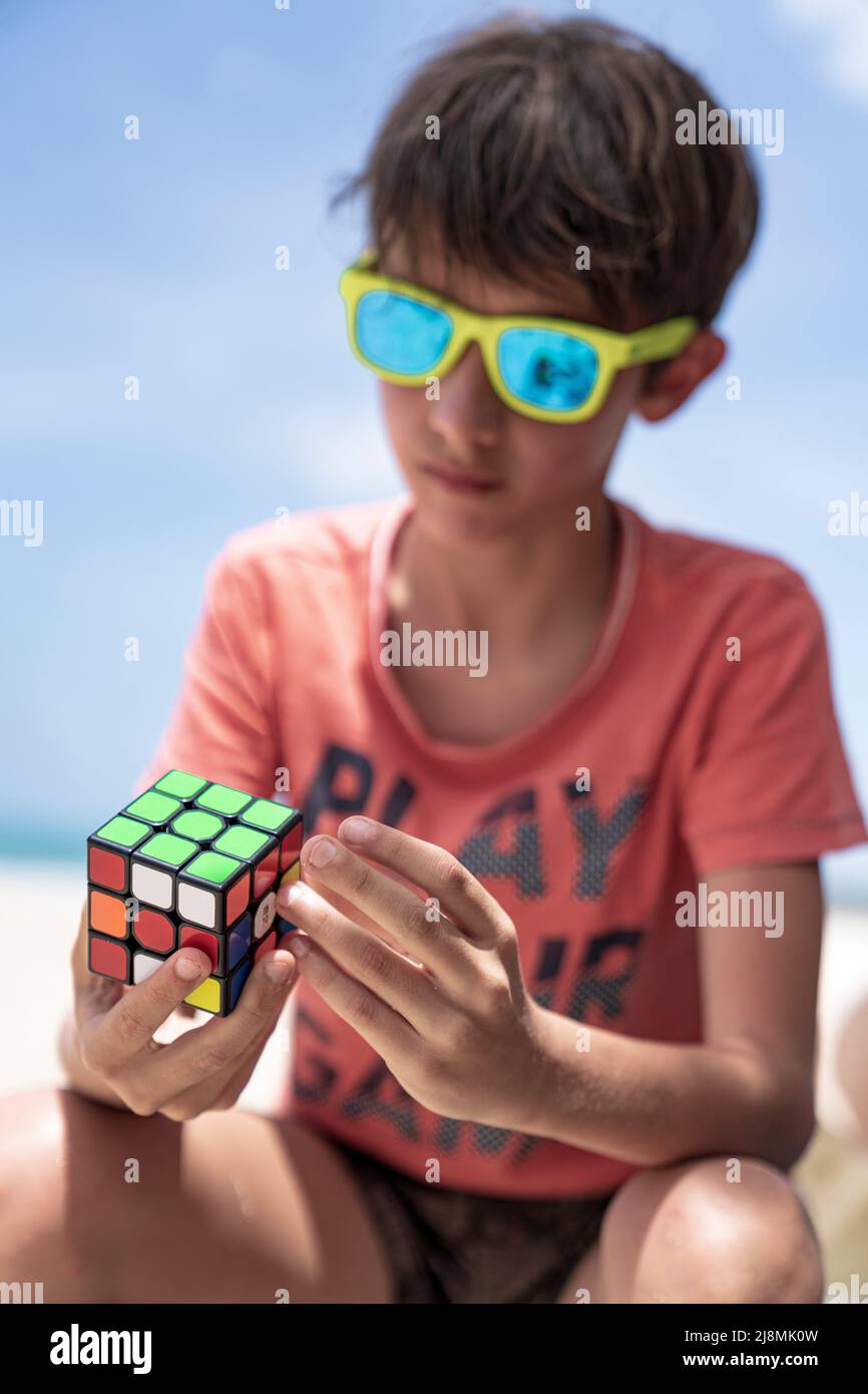 Lindo niño que se divierte jugando con famoso juguete de inteligencia conocido como cubo de Rubik, Antigua, Caribe, West Indies Foto de stock