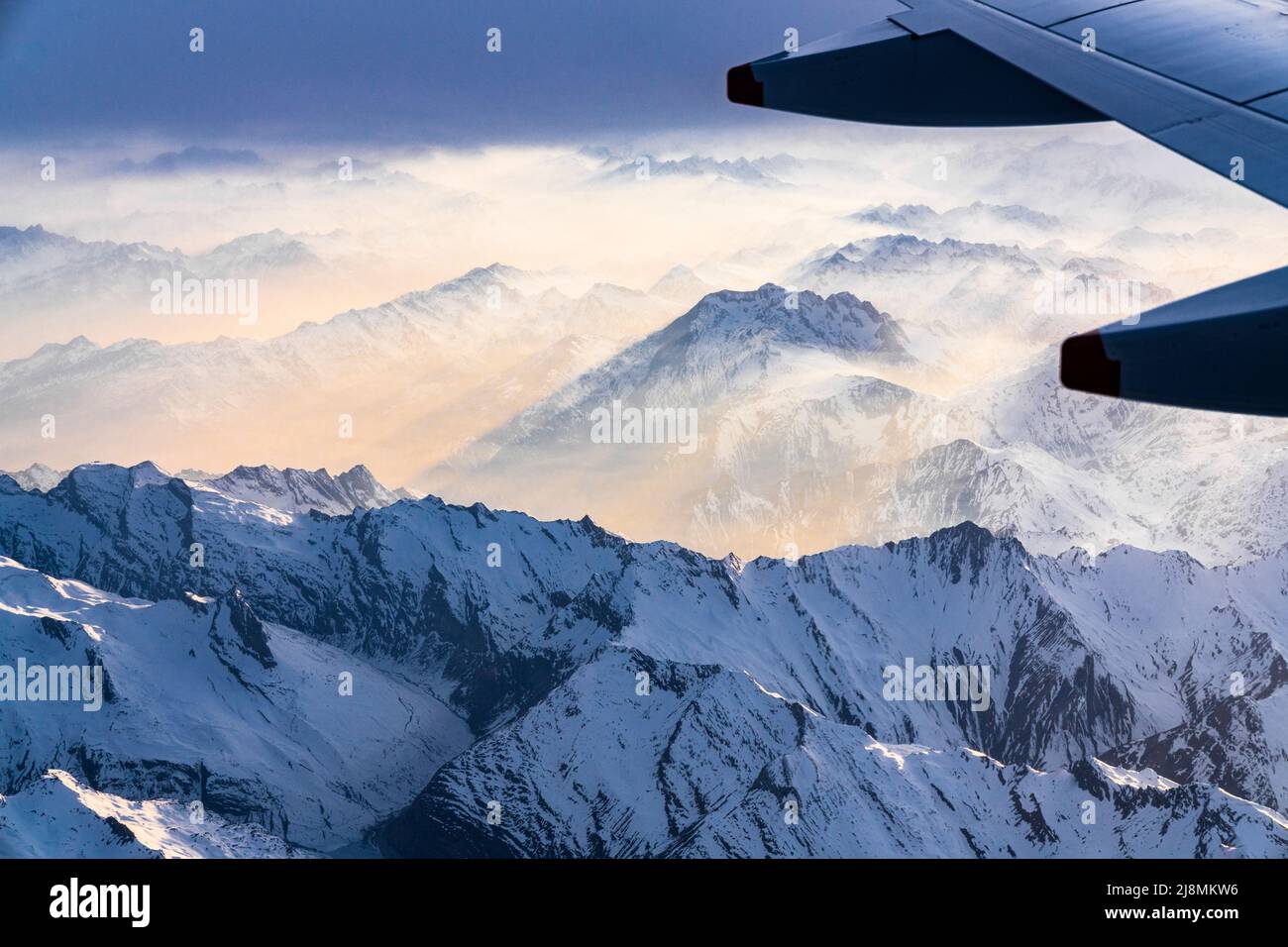 Avión volando sobre Lepontine y los Alpes Ticino cubiertos de nieve durante una puesta de sol foggy, cantón de Graubunden, Suiza Foto de stock