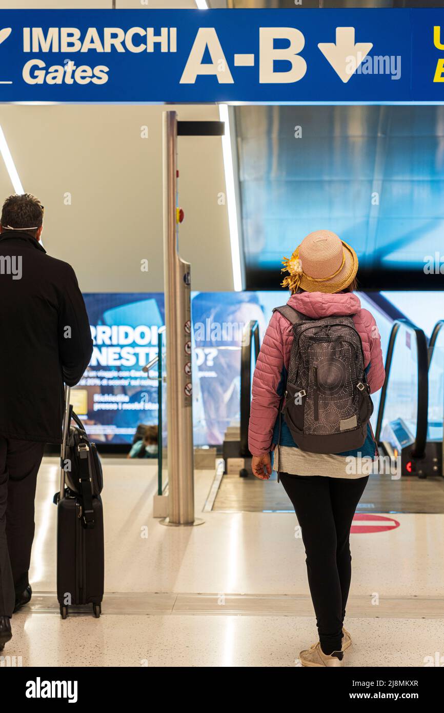 Mujer con mochila y sombrero de paja acercándose a la puerta de embarque en la terminal de salida del aeropuerto Foto de stock