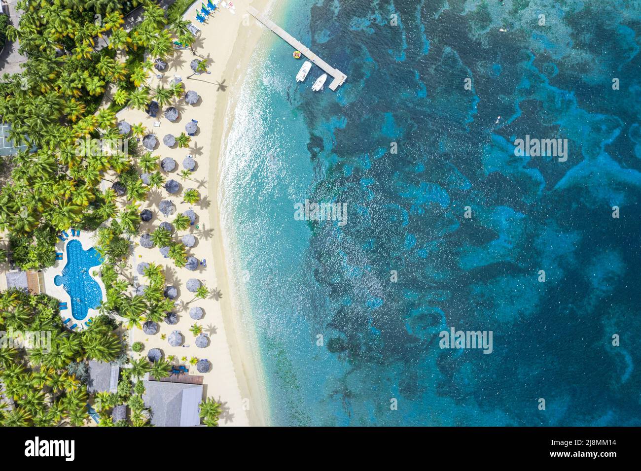 Vista aérea del complejo de lujo con piscina en una playa rodeada de palmeras tropicales junto al azul Mar Caribe, Antigua, West Indies Foto de stock