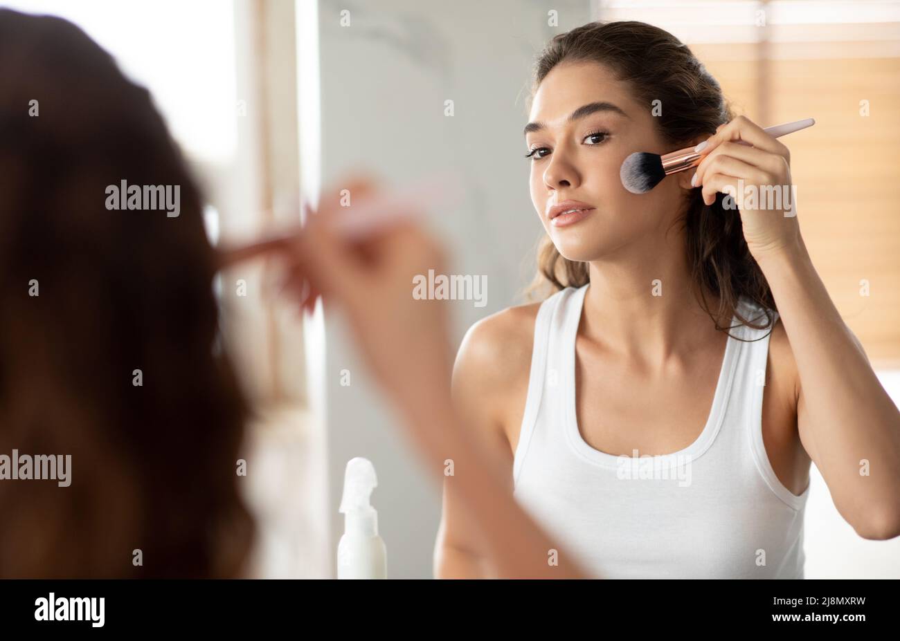 Mujer joven haciendo maquillaje aplicando polvo facial con cepillo en interiores Foto de stock