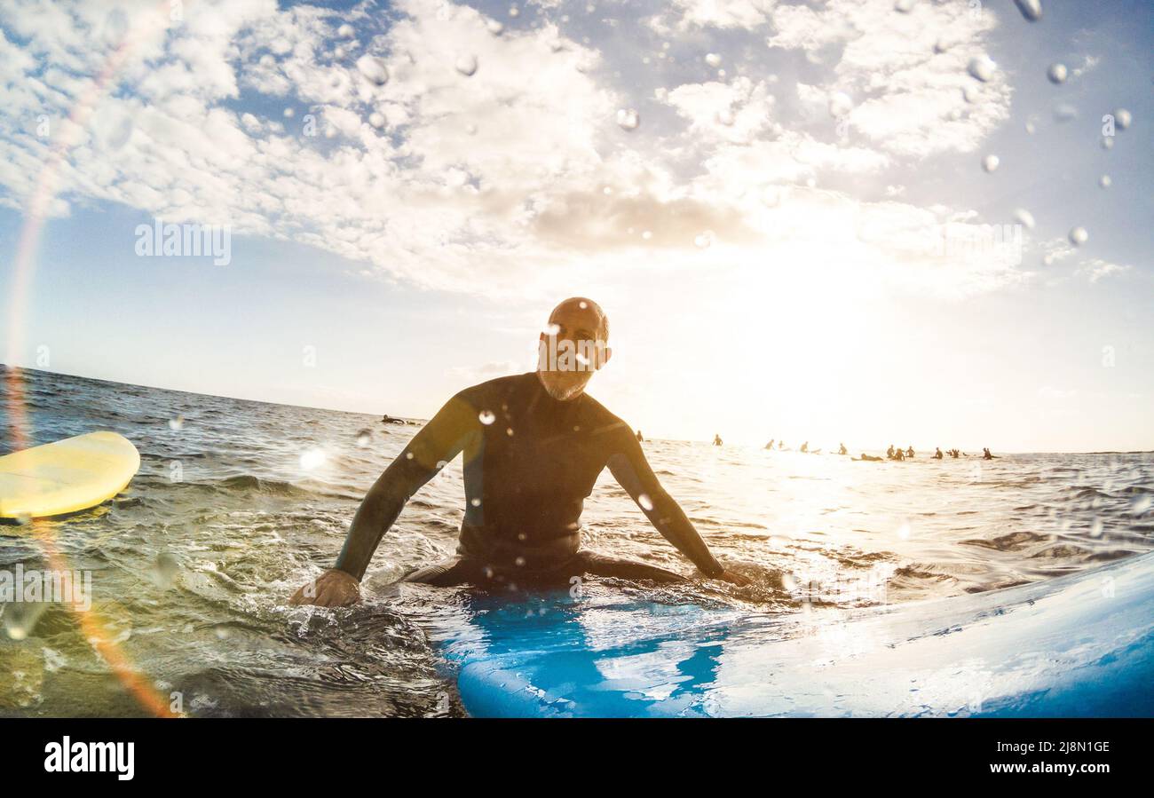 Chico surfista relajarse en la tabla de surf al atardecer en Tenerife con personas irreconocibles en las tablas de surf en el fondo - Concepto de viaje deportivo Foto de stock