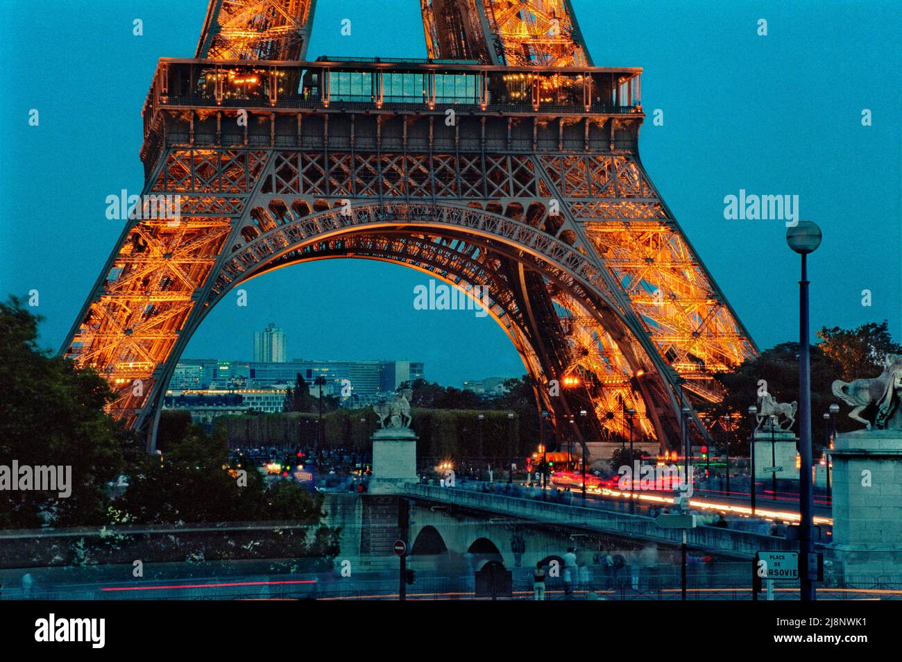 La Torre Eiffel vista desde el otro lado del río Sena: Los visitantes deambulan por debajo de la Torre y cruzando pont d’Iéna en una tarde de verano temprano. Foto de stock