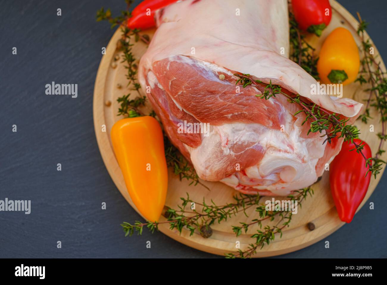 Carne de cerdo sobre el hueso, pimienta fresca dulce y hierba de tomillo sobre una tabla de madera redonda sobre un fondo de pizarra. Productos cárnicos. Foto de stock
