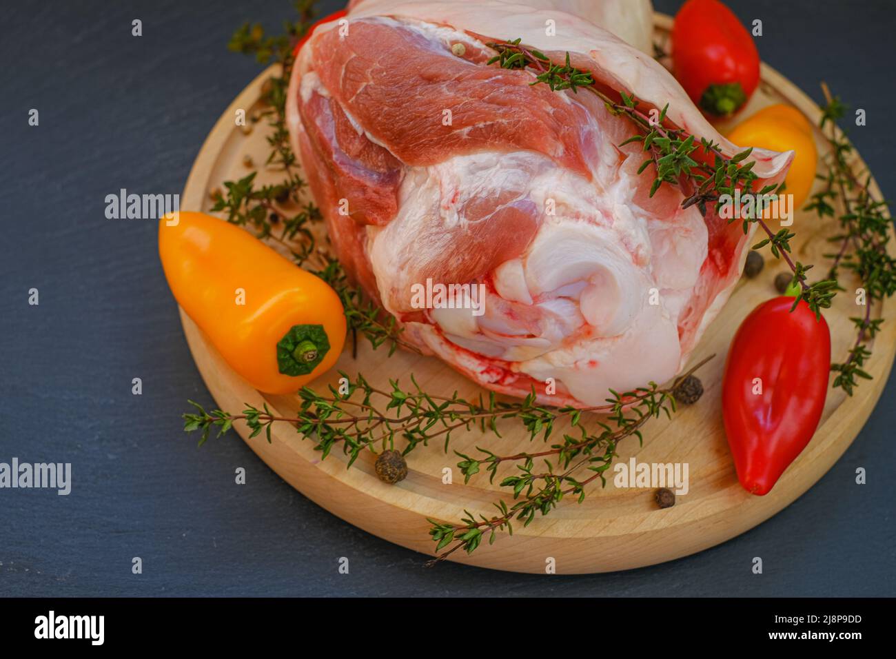 Carne de cerdo en el hueso, pimienta dulce fresca y hierba de tomillo en una tabla redonda sobre fondo de pizarra. Productos cárnicos. Foto de stock