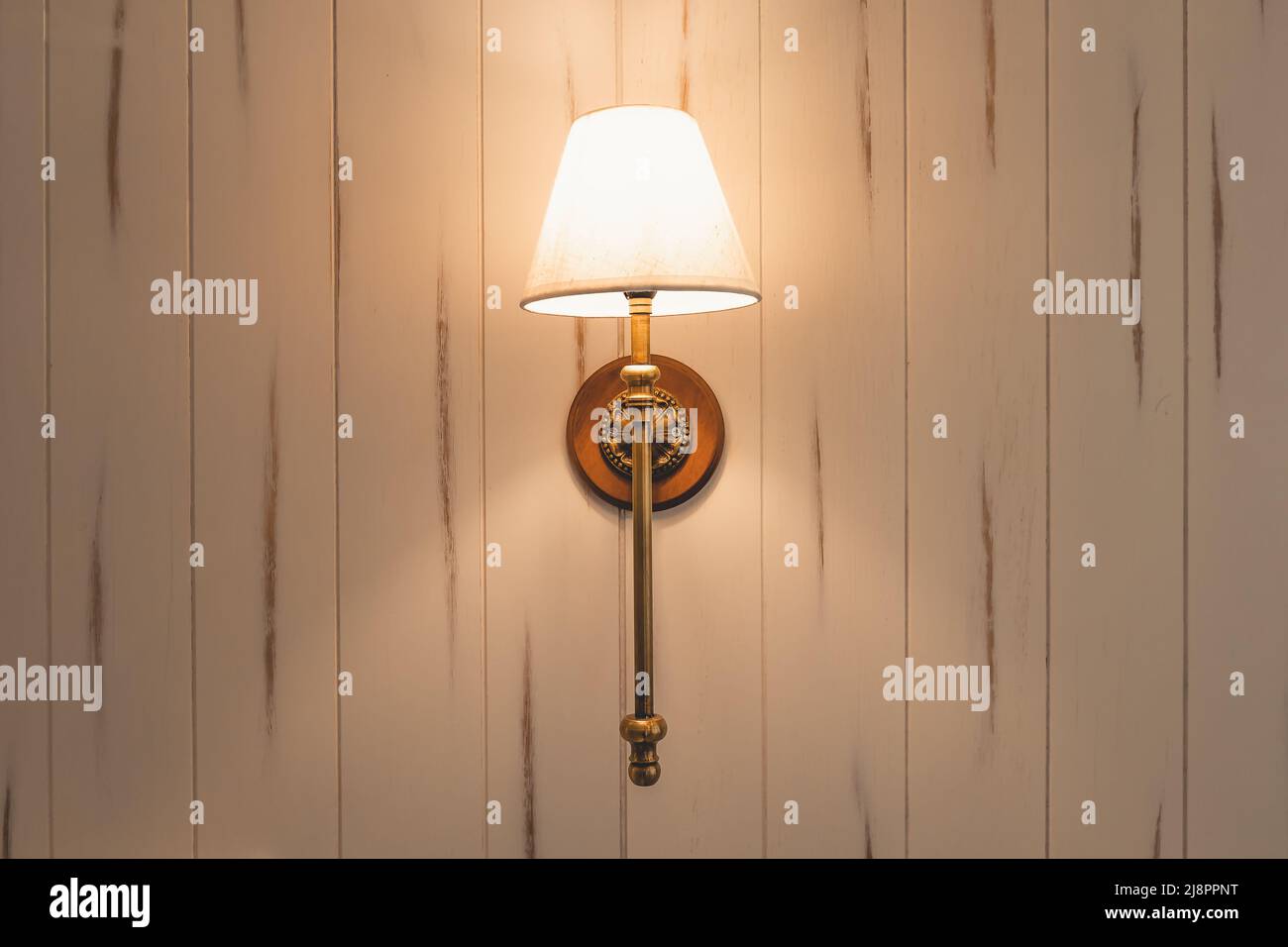 Lámpara de pared en pared de madera con luz cálida en el dormitorio. Foto de stock