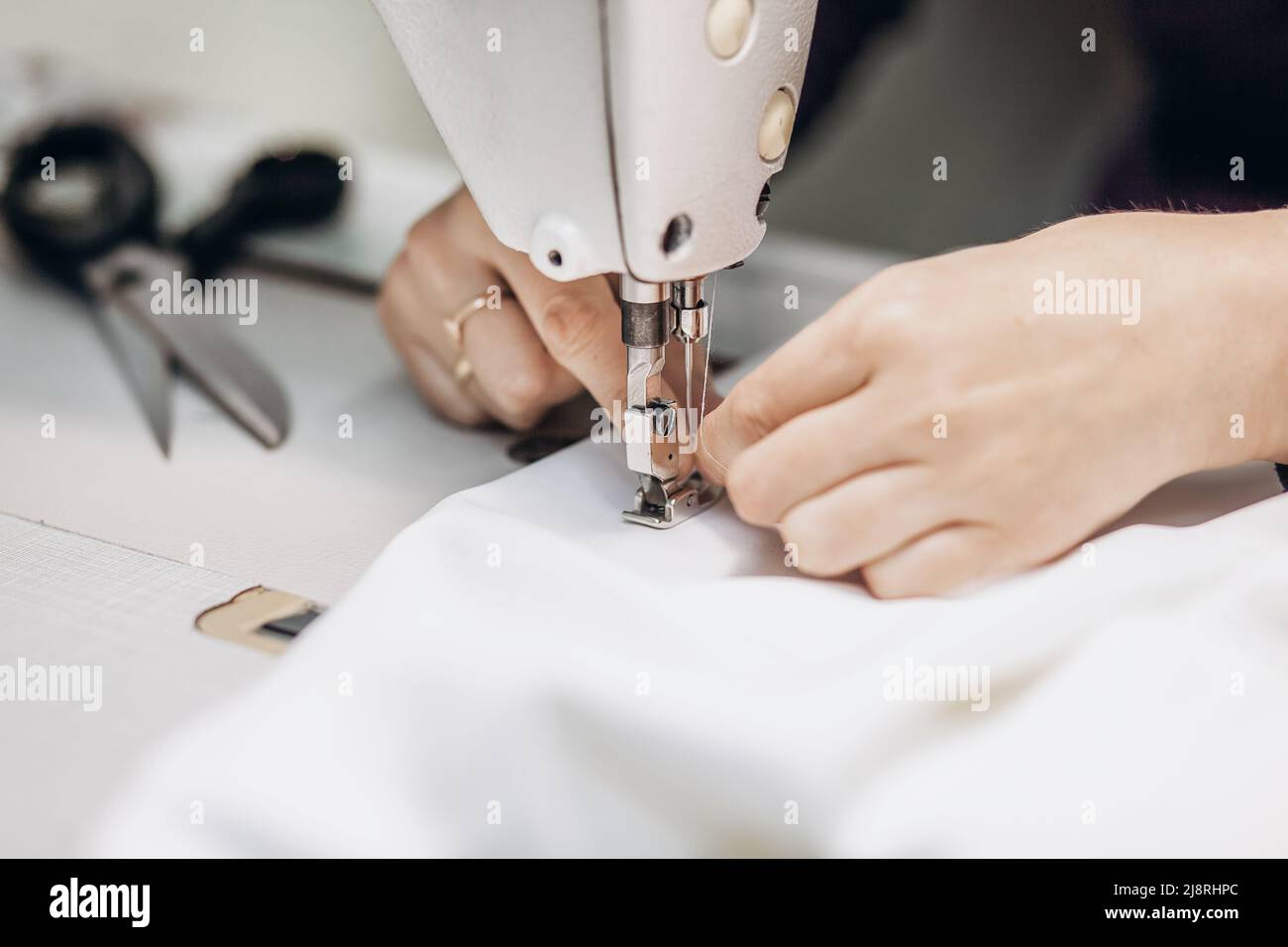 Manos de un fabricante de ropa de costura de tela blanca en una máquina de coser, primer plano. Foto de stock