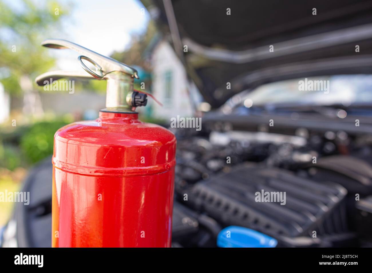 Un extintor de incendios en polvo para automóviles está en un automóvil con  una cubierta abierta. El concepto de extintores modernos para extinguir un  incendio en un coche. Espacio de copia f