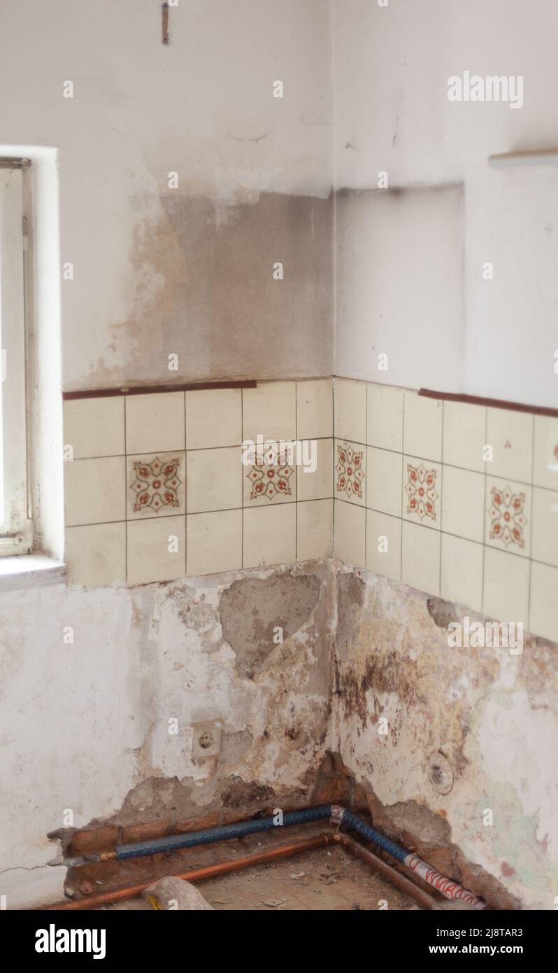 Detalle de una habitación con una vieja pared húmeda, nuevas tuberías de calefacción de cobre y azulejos viejos Foto de stock