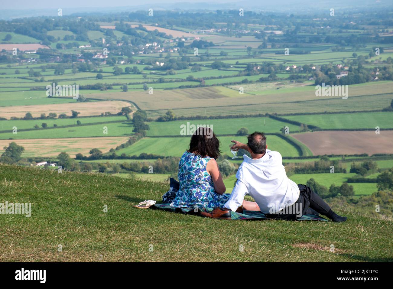 Una pareja de mediana edad picnic en Glastonbury Tor con una vista sobre los niveles de Somerset Foto de stock