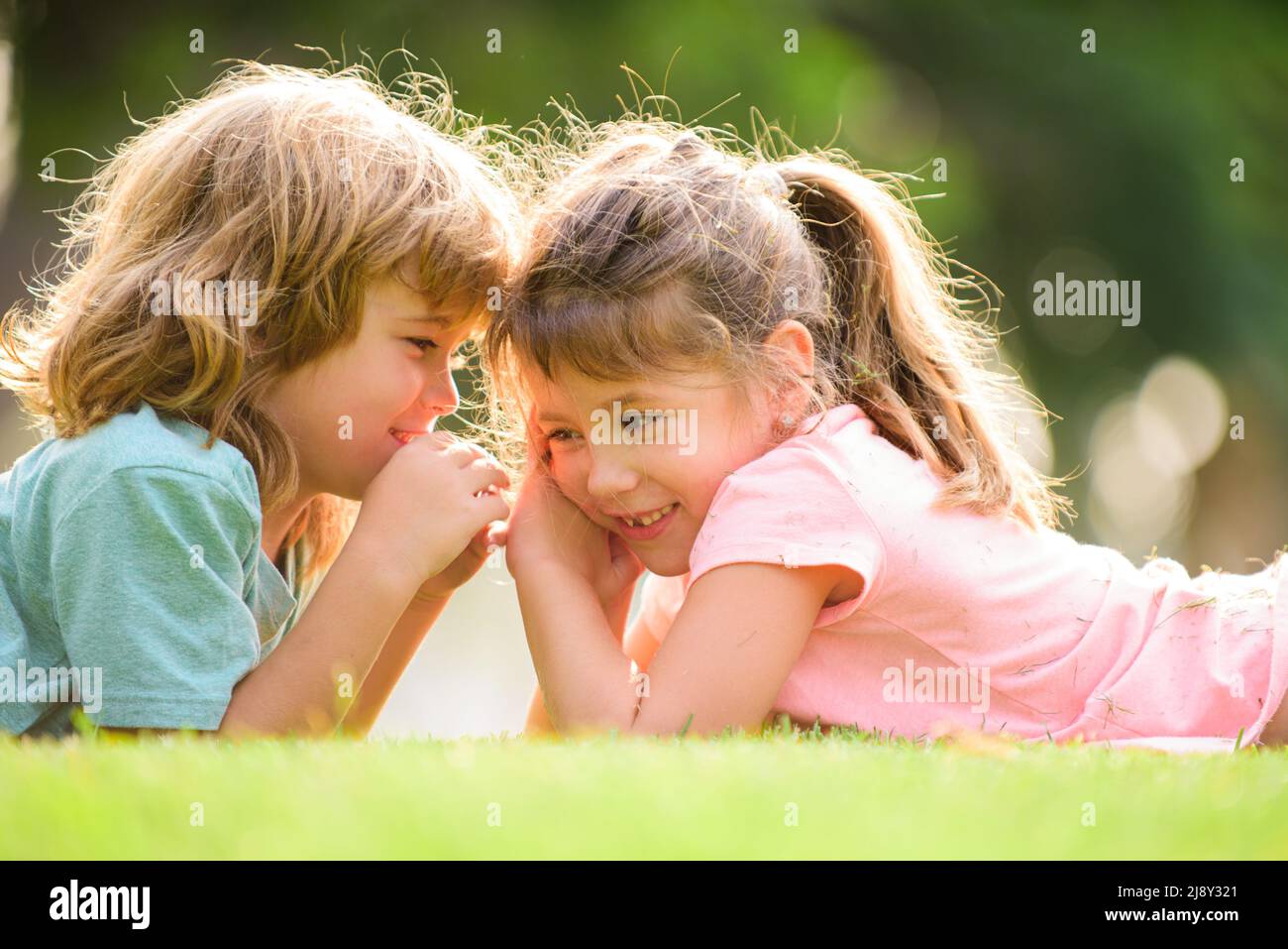 Niño y niña mejor amigos abrazando. Los niños se besan unos a otros con amor en el parque de verano. Amigos pequeños. Rubia niños hermano y hermana acostado Foto de stock