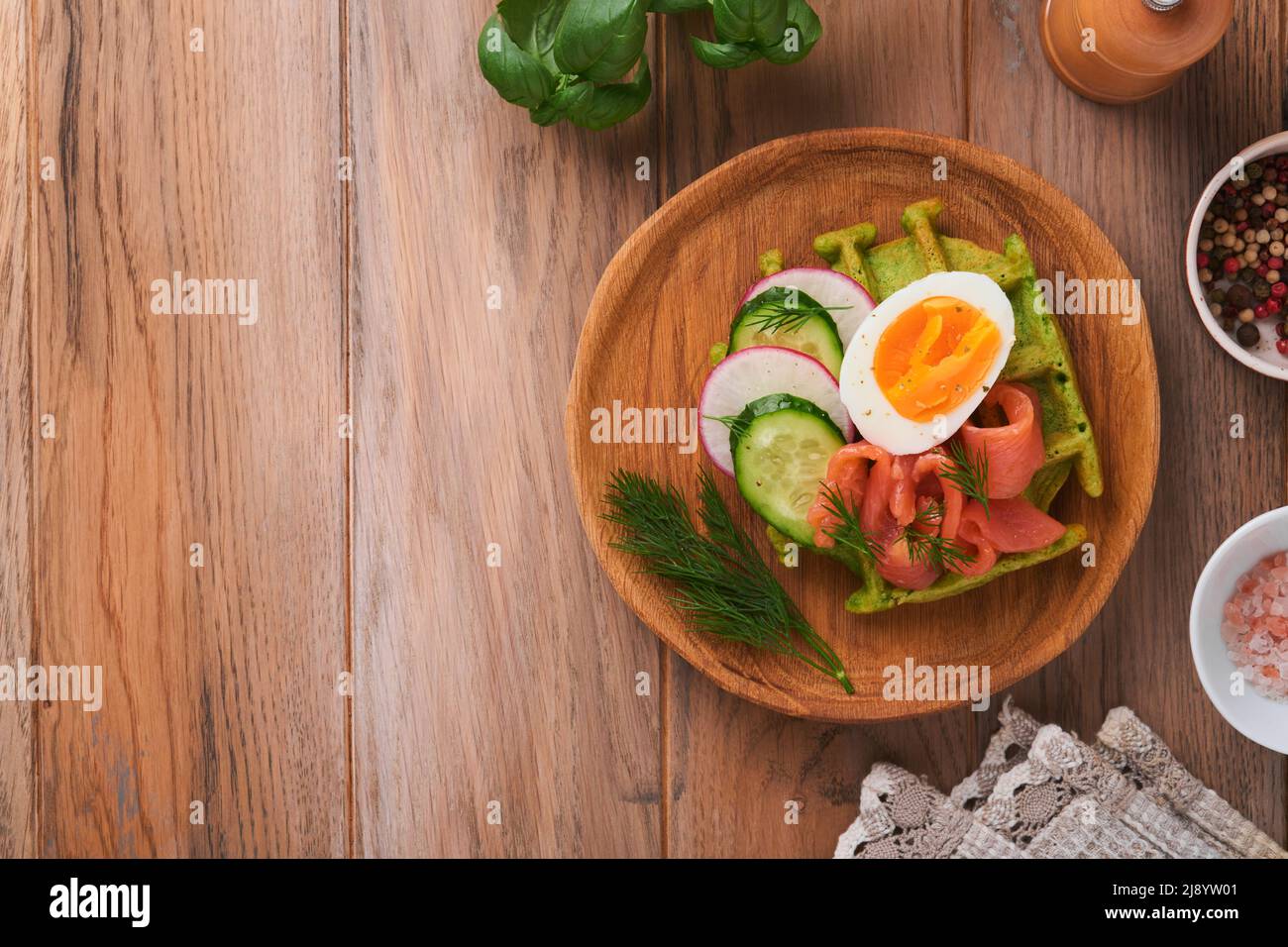 Gofres salados. Desayuno con gofres verdes, ajo o espinacas silvestres con huevo, tomate y salmón sobre plato de madera para el desayuno sobre el fondo de madera antiguo. Luz Foto de stock