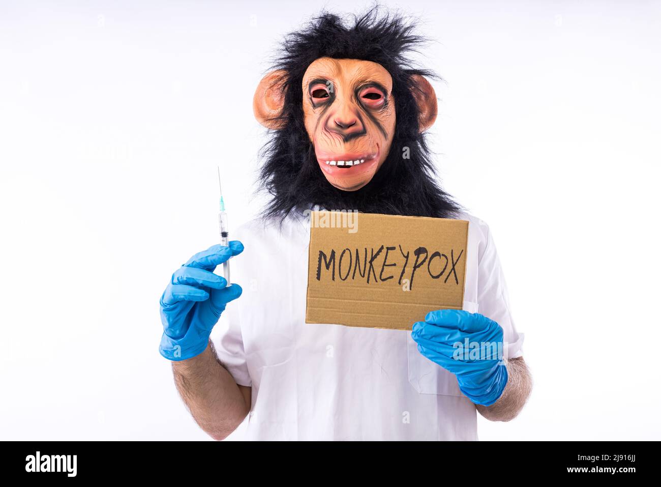 Persona vestida en una máscara de mono, en un traje de enfermera médica,  sosteniendo un cartel con el signo de peligro y un mono, que dice: VIRUELA  DEL SIMIO, en una espalda