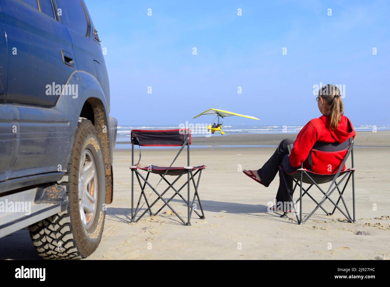 Mujer sentada en silla de camping junto a un vehículo todoterreno en la playa viendo un avión ligero despegando, ULM, Torres, Rio Grande do Sul, Brasil Foto de stock