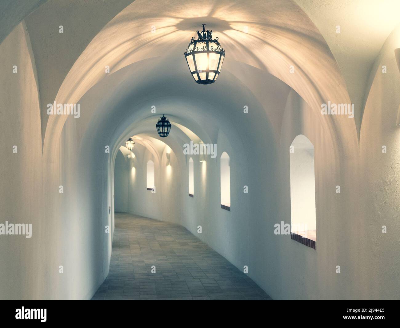Pasillo del castillo iluminado con la iluminación del techo. Interior de un largo pasillo con paredes blancas y arcos, enfoque selectivo Foto de stock