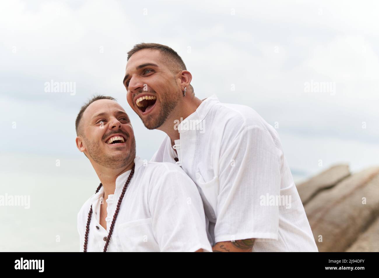 Pareja gay riendo distraído mientras se abraza en la playa Foto de stock