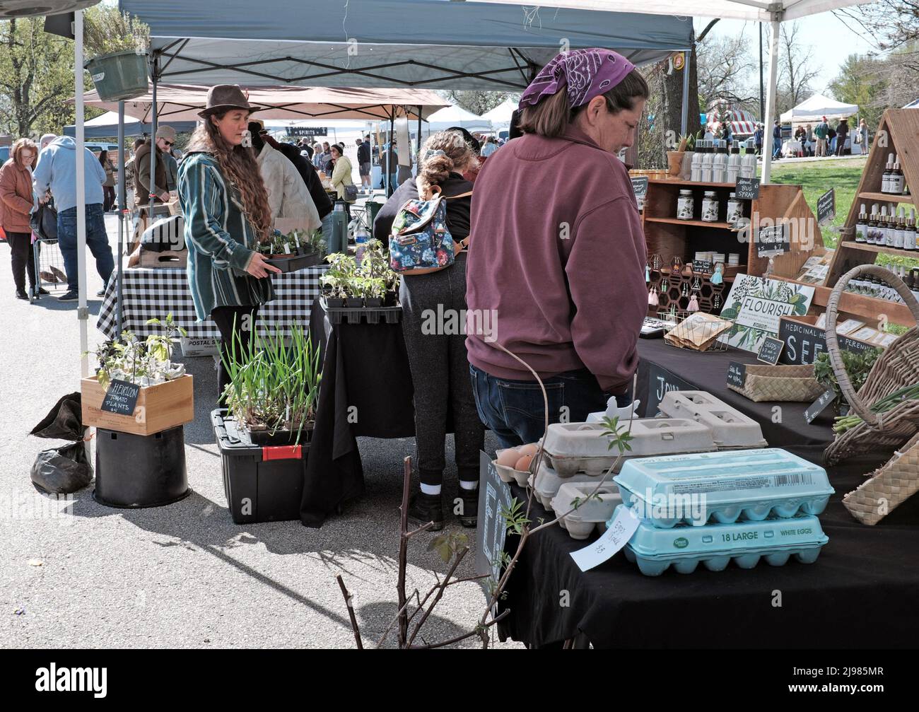 Un vendedor femenino observa a dos hembras que perusan los bienes para la venta durante el mercado de granjeros de Tower Grove el 16 de abril de 2022 en St. Louis, MO, USA. Foto de stock