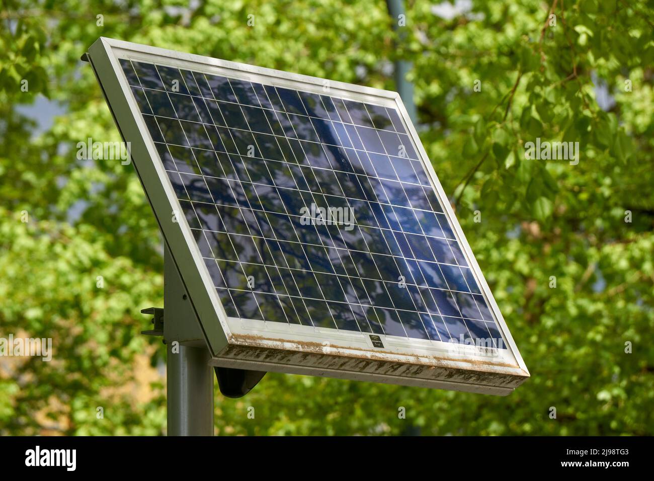 Primer plano de un único panel solar montado sobre un soporte con árboles verdes en el fondo Foto de stock