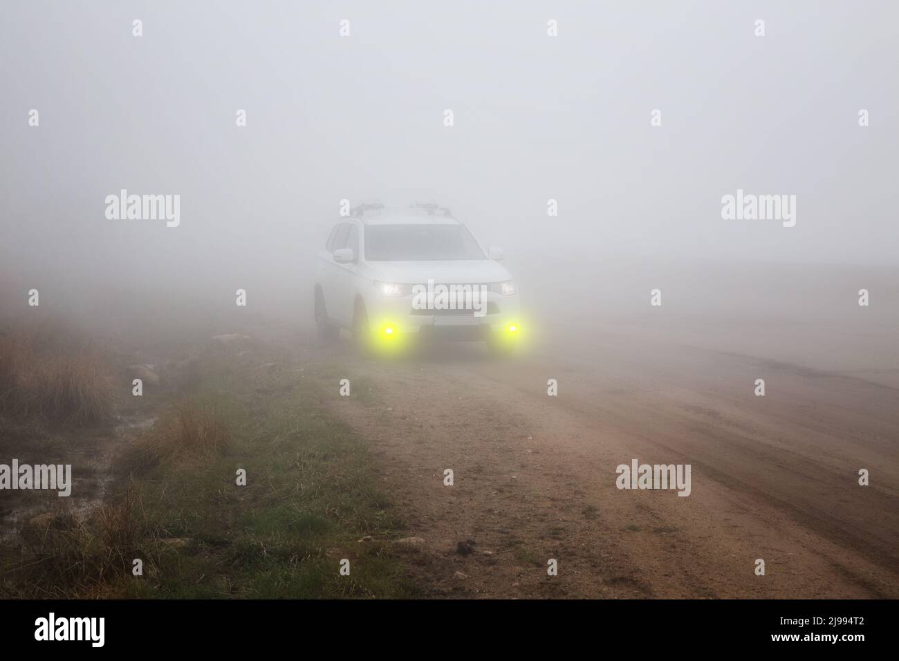 Coche SUV blanco con luces amarillas de niebla en una carretera de montaña en niebla espesa Foto de stock