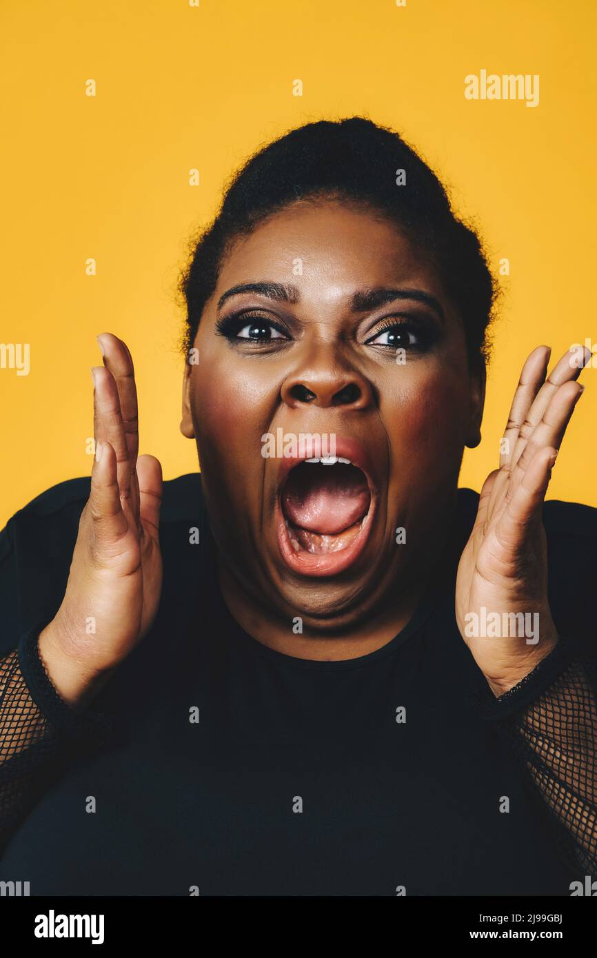primer plano retrato de una joven mujer adulta negra en shock con boca abierta gritando en el estudio de fondo amarillo Foto de stock
