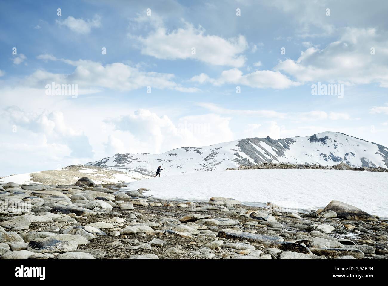 Hombre con mochila caminando en la colina de nieve en las hermosas montañas contra el cielo azul en Almaty, Kazajstán Foto de stock