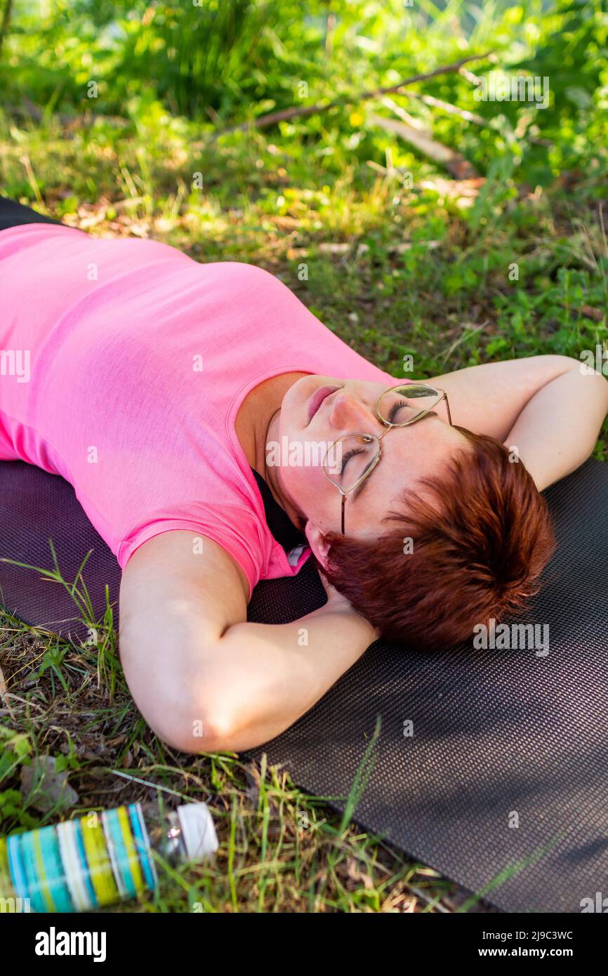 Hermosa mujer joven sonriendo y soñando tumbada en el suelo después de hacer ejercicio en un cálido día de verano Foto de stock