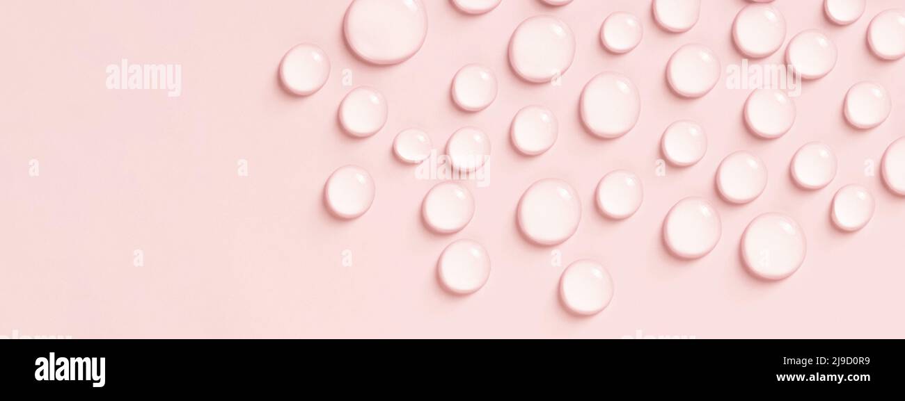 Gotas de agua o líquido cosmético sobre fondo rosa. Foto de stock