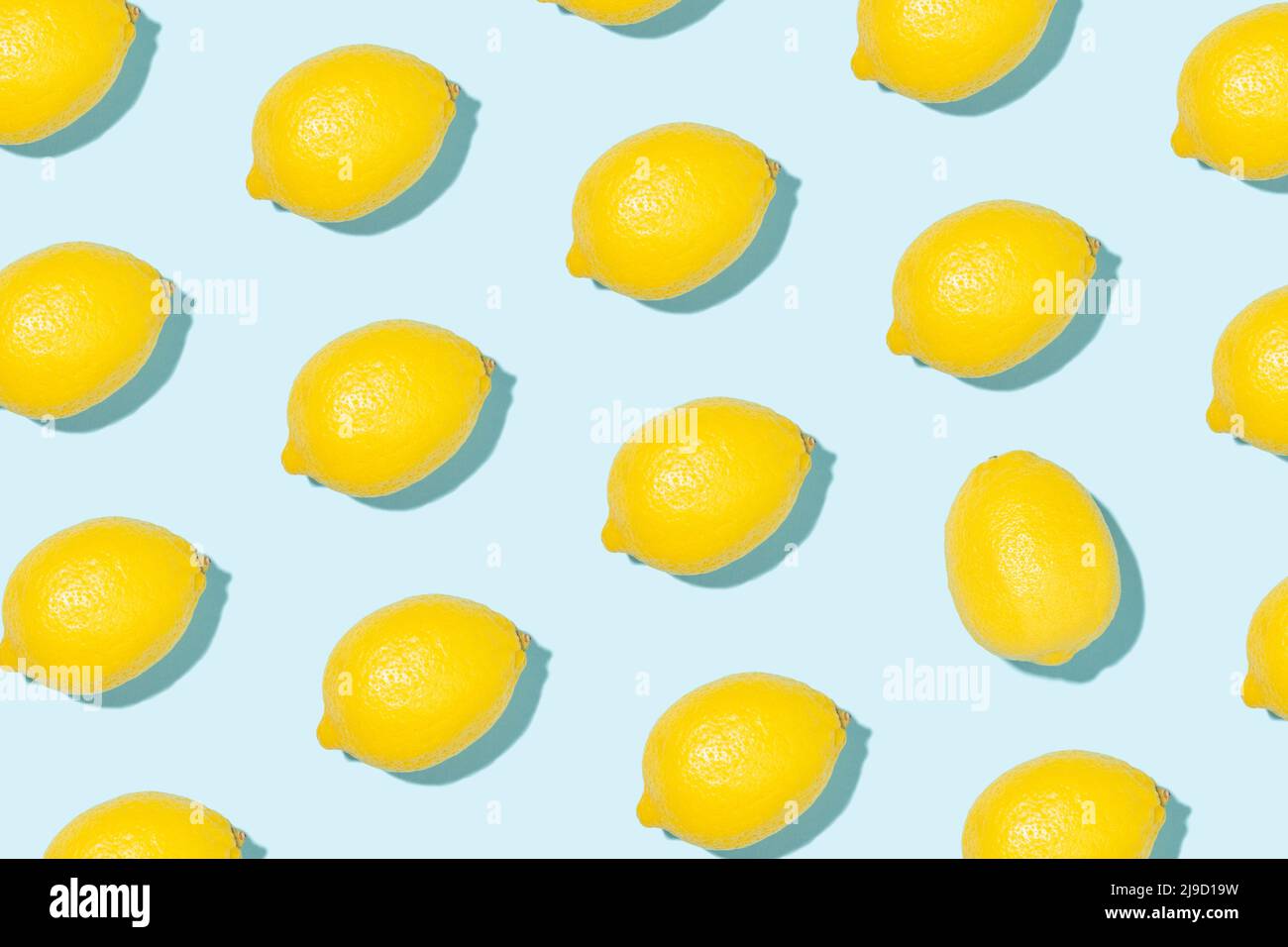 Patrón hecho de limones amarillos brillantes en la luz del sol sobre fondo azul. Concepto de verano de estilo minimalista. Foto de stock
