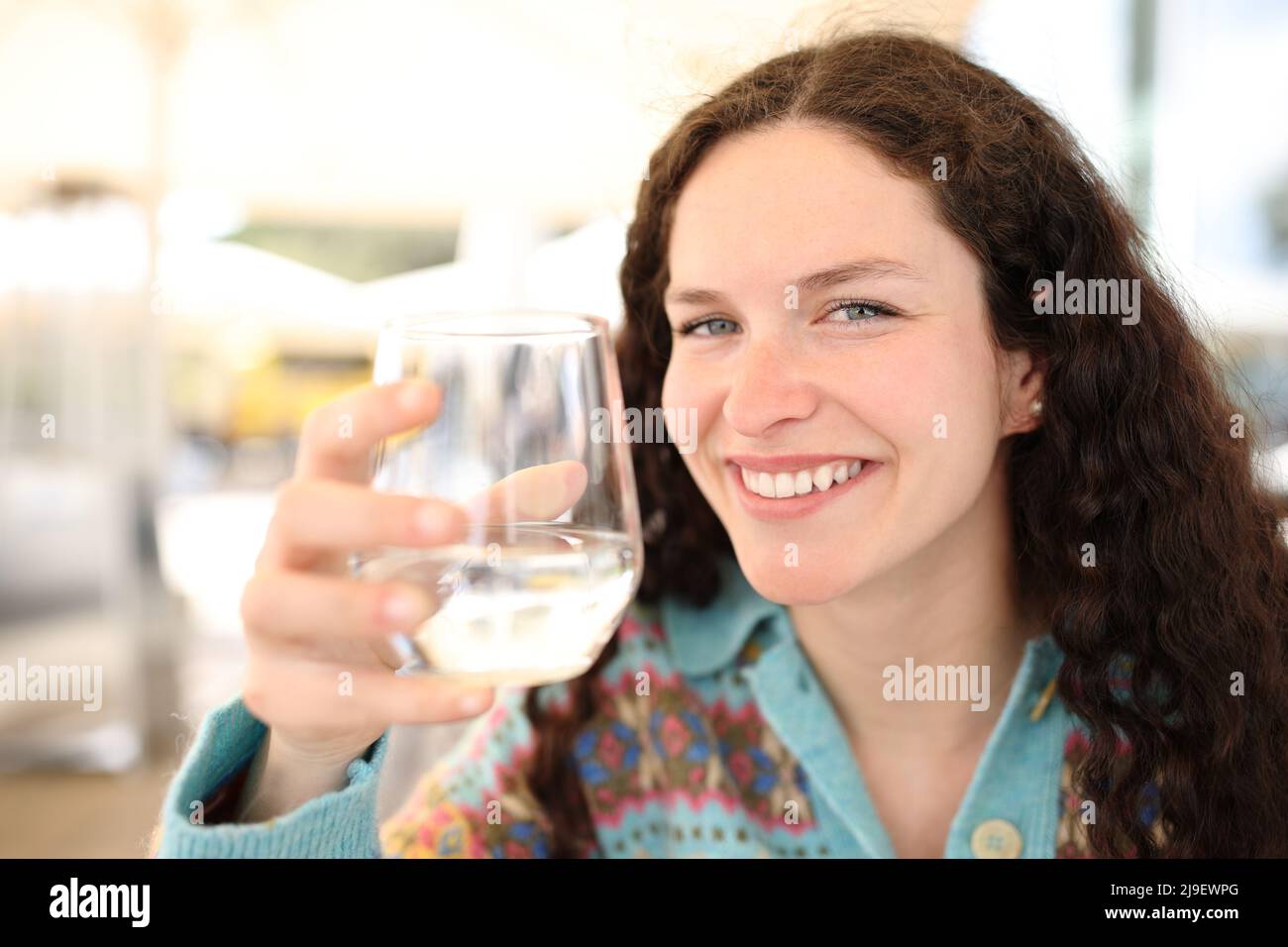 Una mujer feliz sosteniendo un vaso de agua le mira en la terraza del bar Foto de stock
