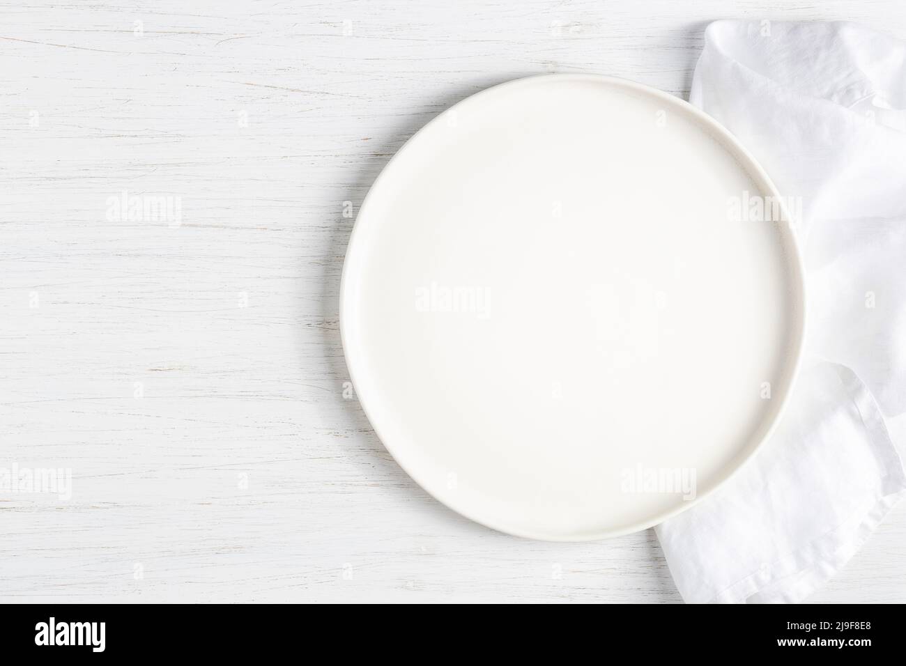 Plato blanco vacío y servilleta de lino sobre mesa de madera blanca. Foto de stock