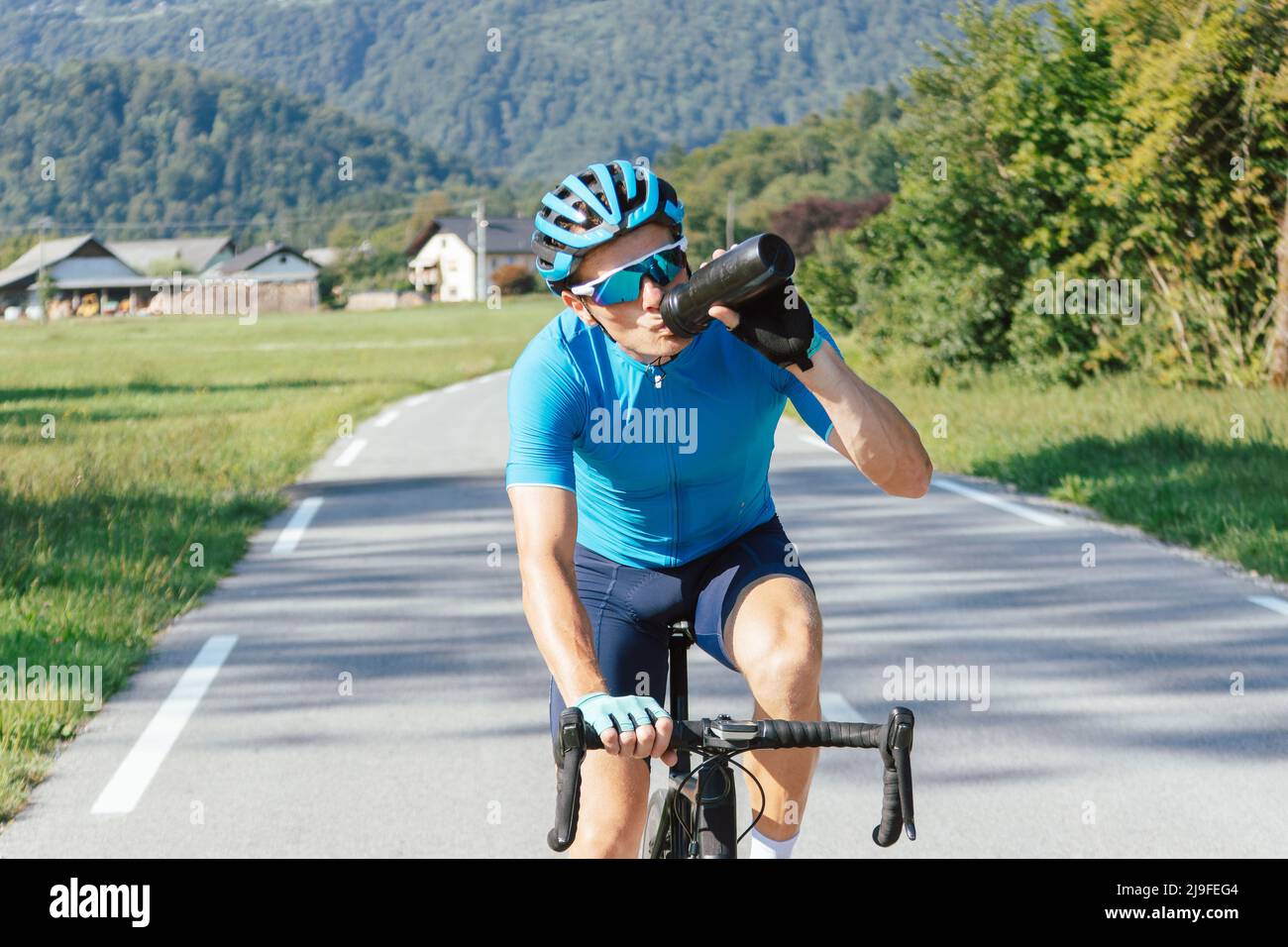 Detenerse Mensajero petróleo El ciclista caucásico masculino de carreras de bicicletas en la camiseta  deportiva azul bebe agua de una botella mientras monta, vista frontal  Fotografía de stock - Alamy