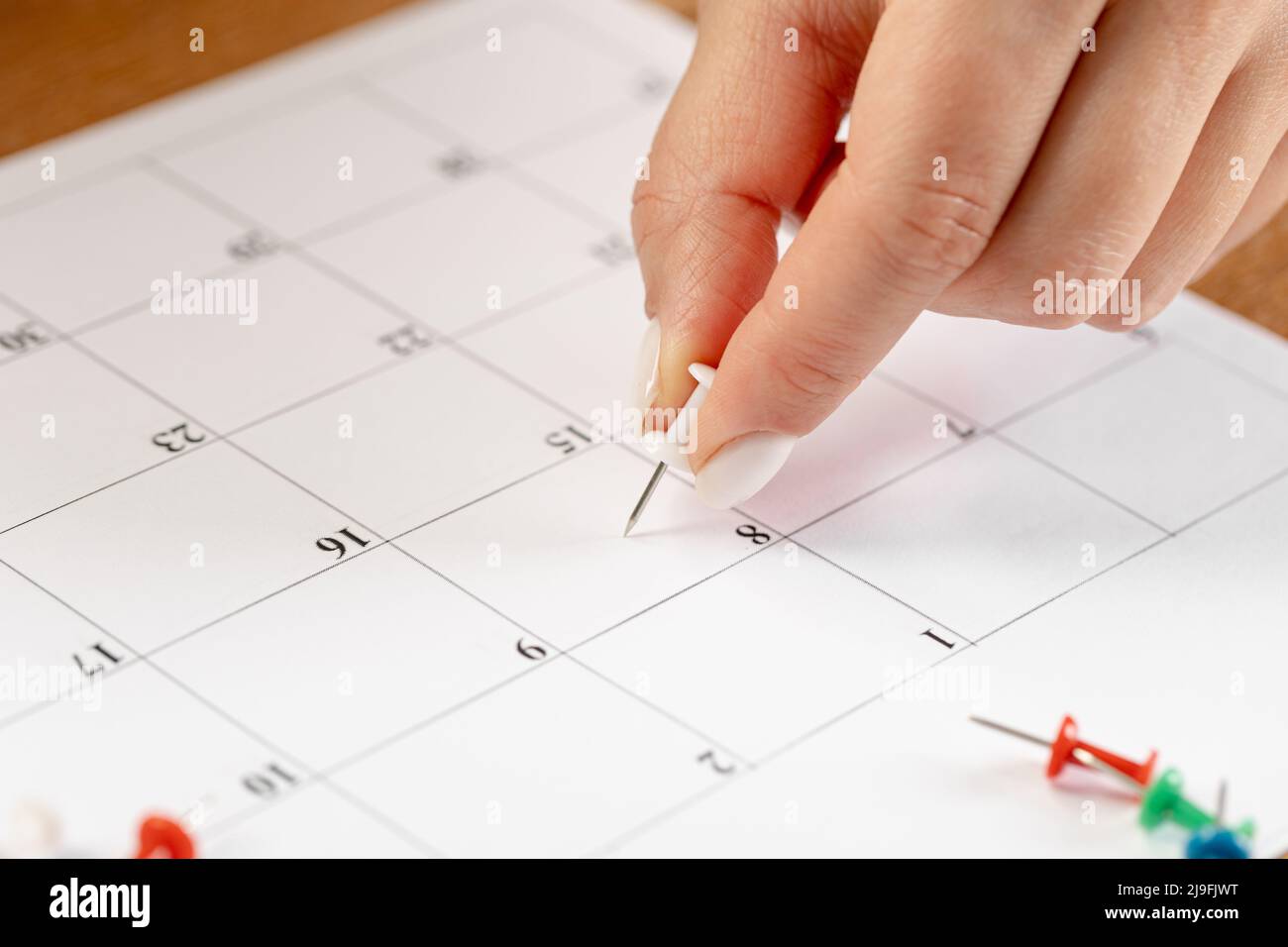 Programación de notas de fijación de manos, miniatura de pin blanco en el calendario para reuniones y recordatorios de citas Foto de stock