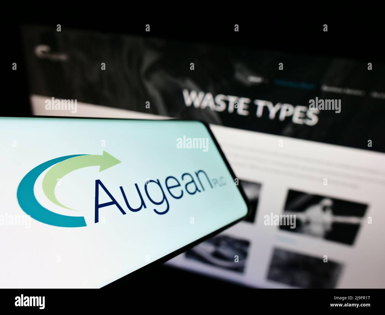 Teléfono móvil con el logotipo de la empresa británica de gestión de residuos Augean plc en la pantalla frente al sitio web empresarial. Enfoque a la izquierda de la pantalla del teléfono. Foto de stock