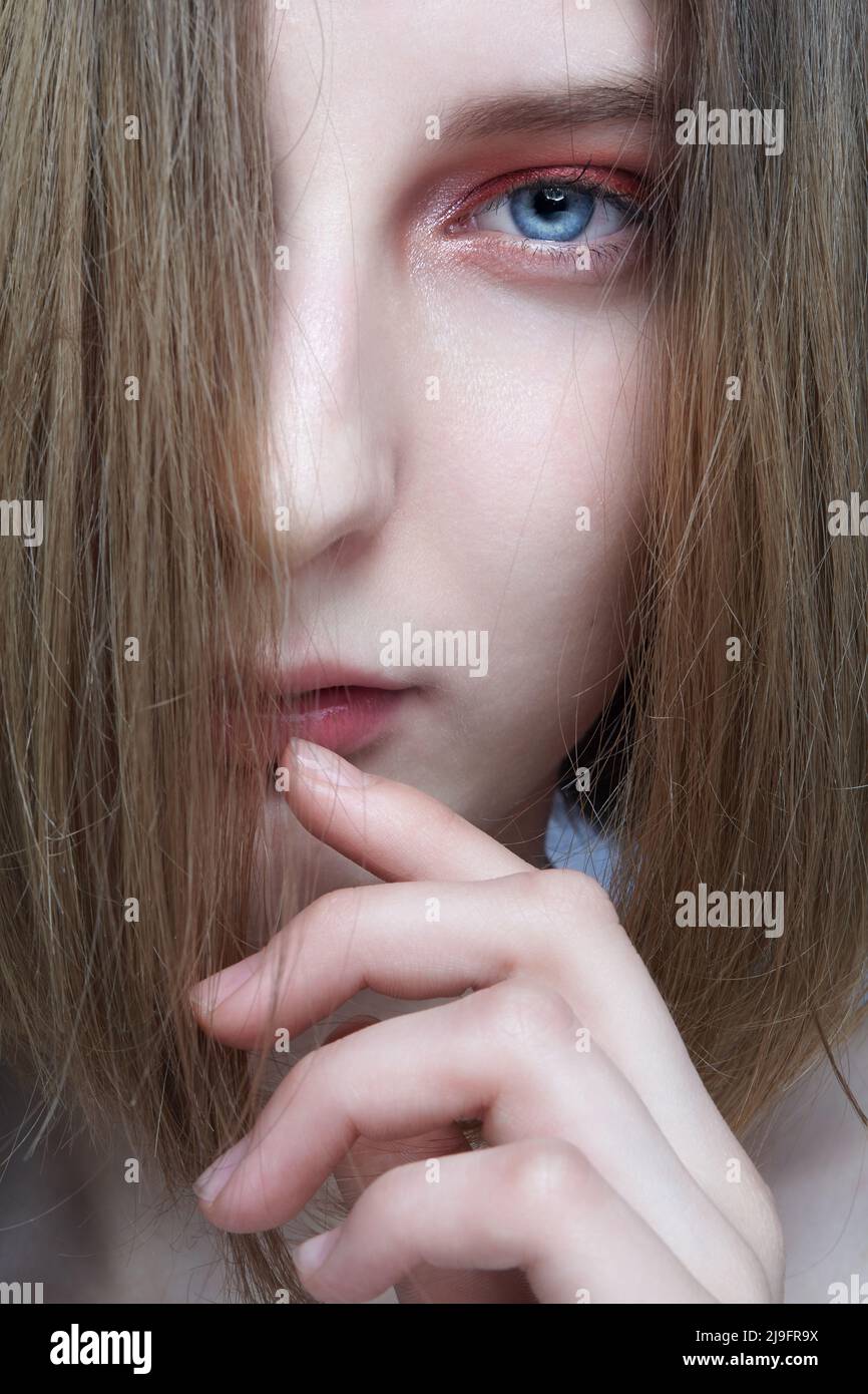 Primer plano retrato de una hermosa mujer joven. Mujer con pelo rubio cubriendo su cara mira a la cámara. Foto de stock