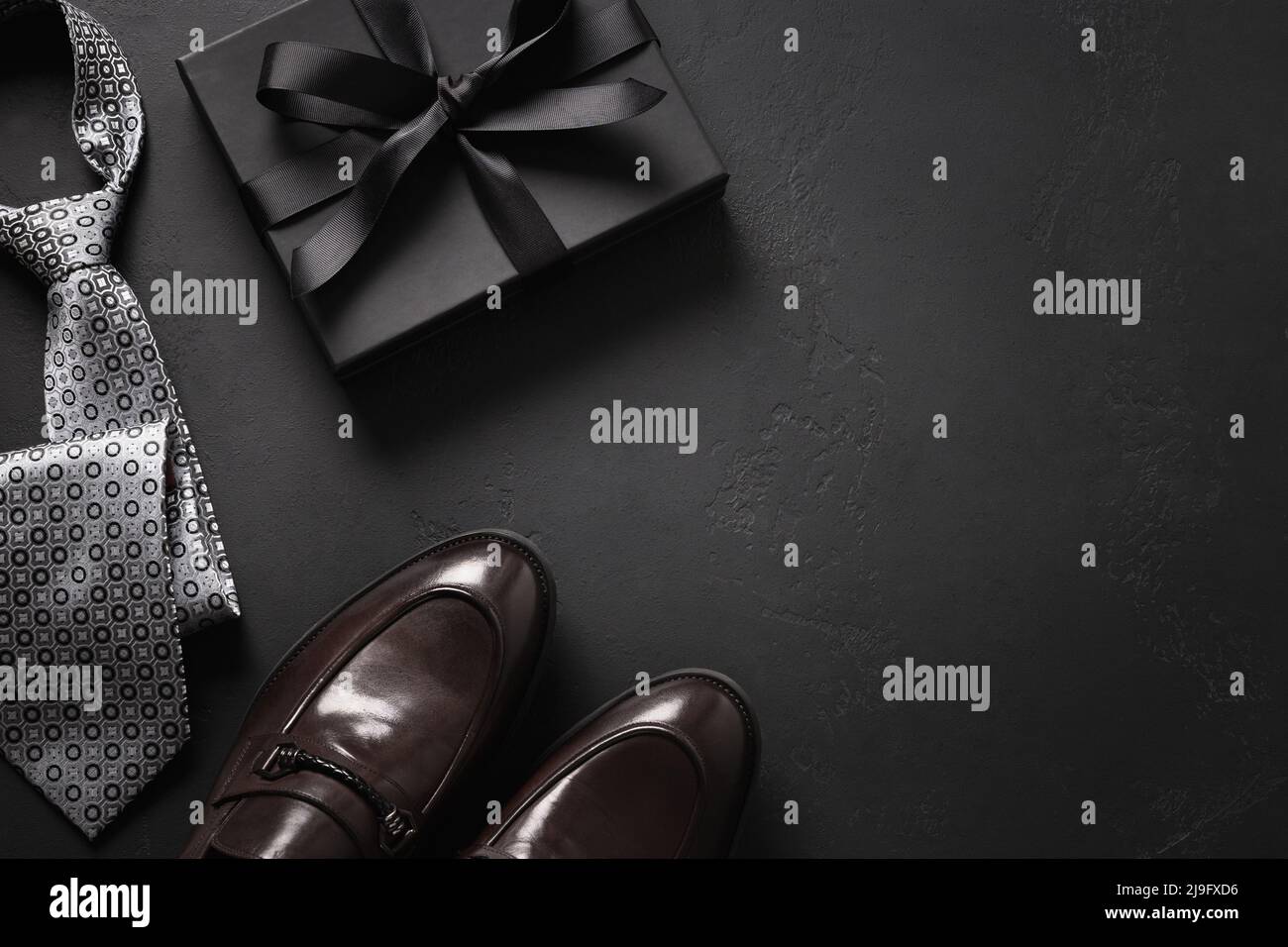 Tarjeta de felicitación para el Día de los Padres con caja de regalo.  Conjunto de ropa clásica para hombre: Zapatos marrones, corbata y regalo  sobre fondo negro. Juego de accesorios para hombre.