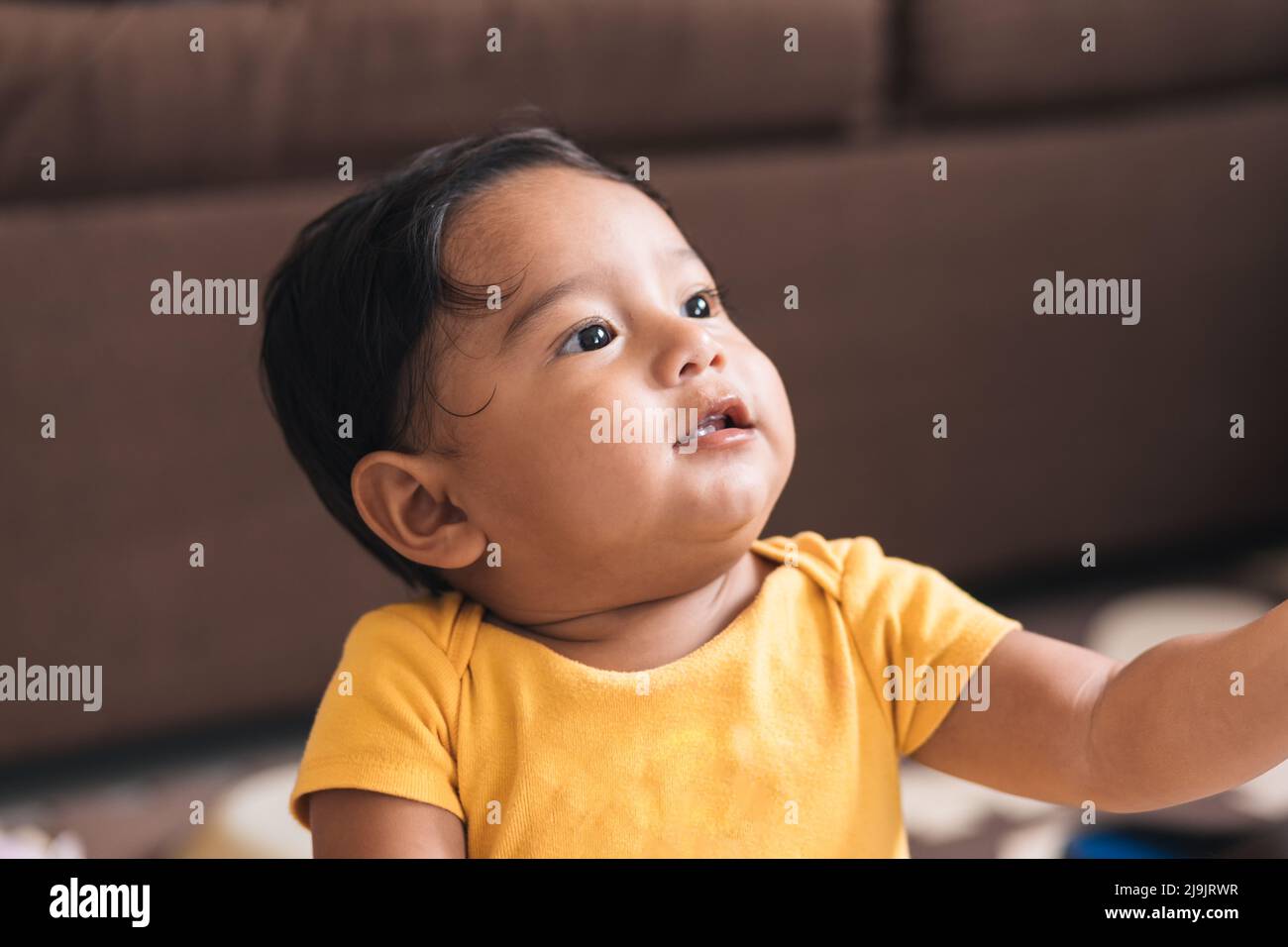 bebé sentado en el suelo mirando hacia arriba Foto de stock