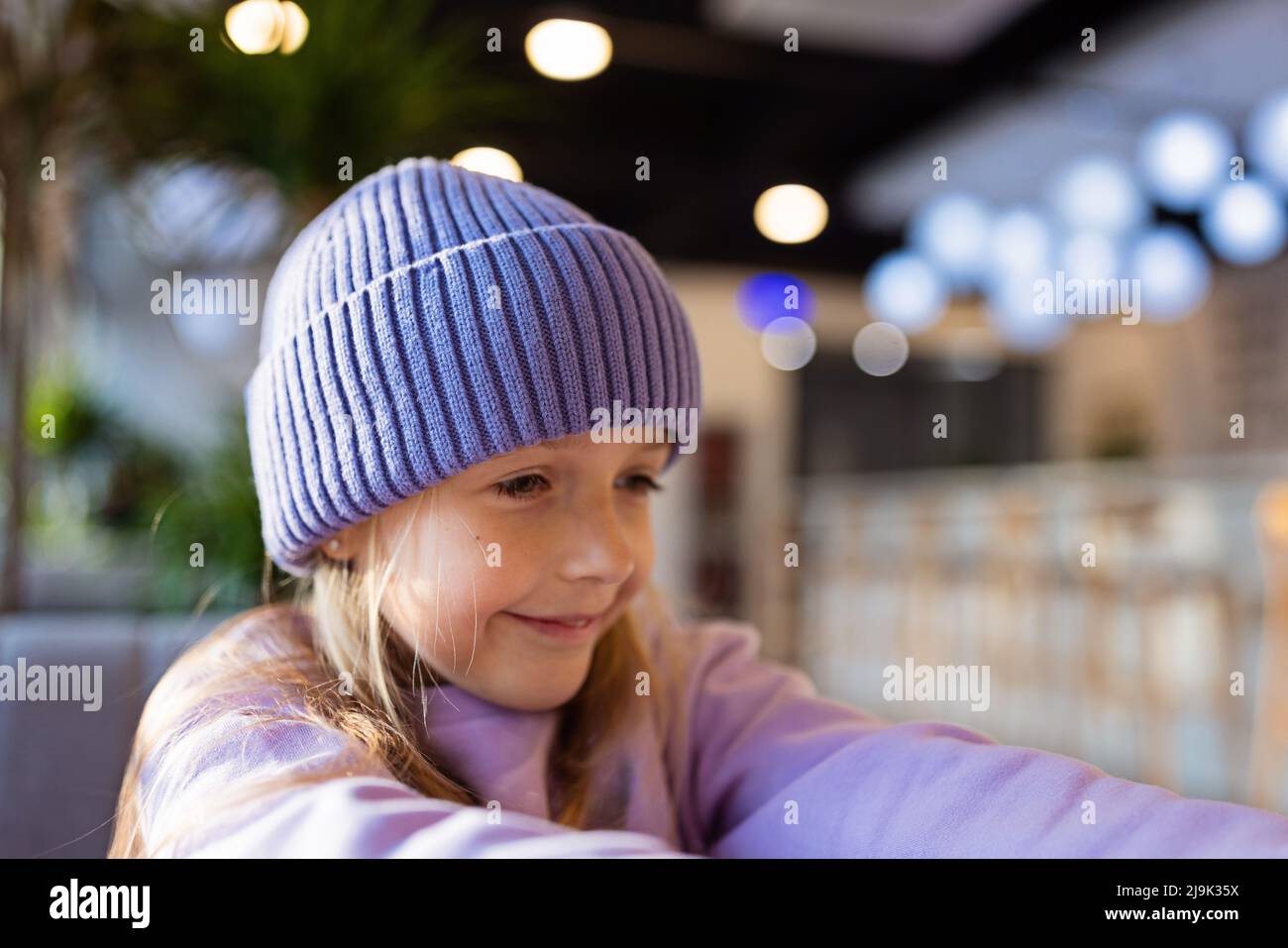 Linda niña caucásica de ocho años con cabello rubio sonriendo en un café  moderno. Niño con camisa con estilo y sombrero de punto de color violeta.  Moderno Fotografía de stock - Alamy