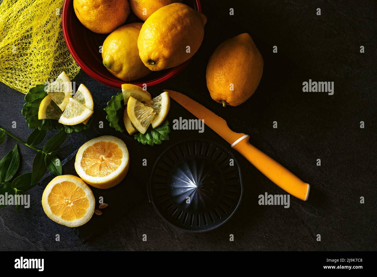 Elegante diseño de fondo de limones y rodajas de limón con exprimidor y cuchillo sobre cemento oscuro o negro o superficie de piedra. Foto de stock