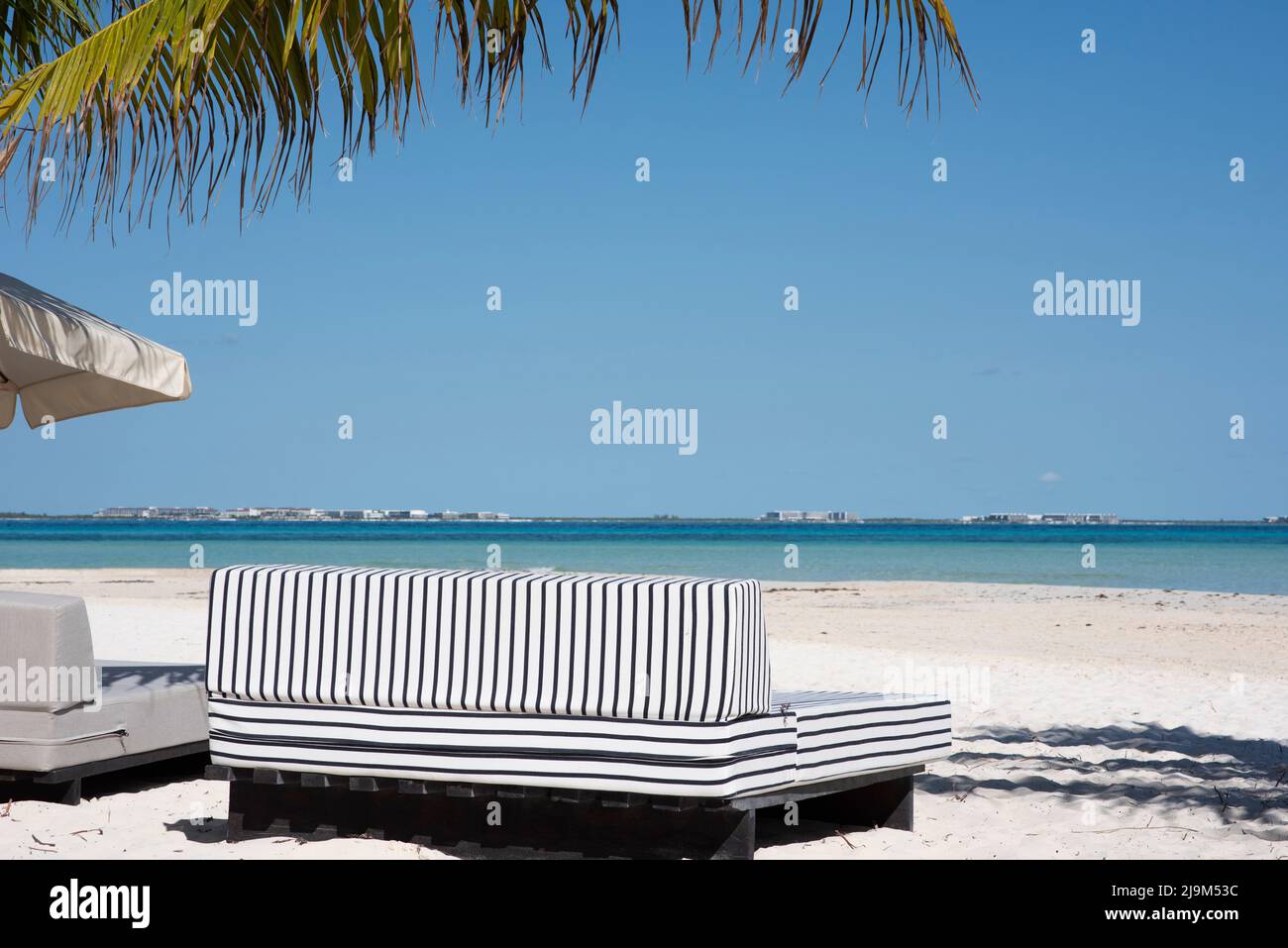 Elegante sofá y sombrilla en una playa tropical con palmeras en Isla Mujeres, México Foto de stock