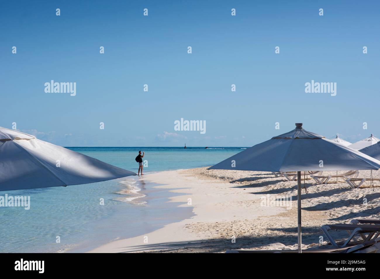 Las sombrillas blancas se abren en una playa tropical, y un turista en el fondo tomando una selfie Foto de stock