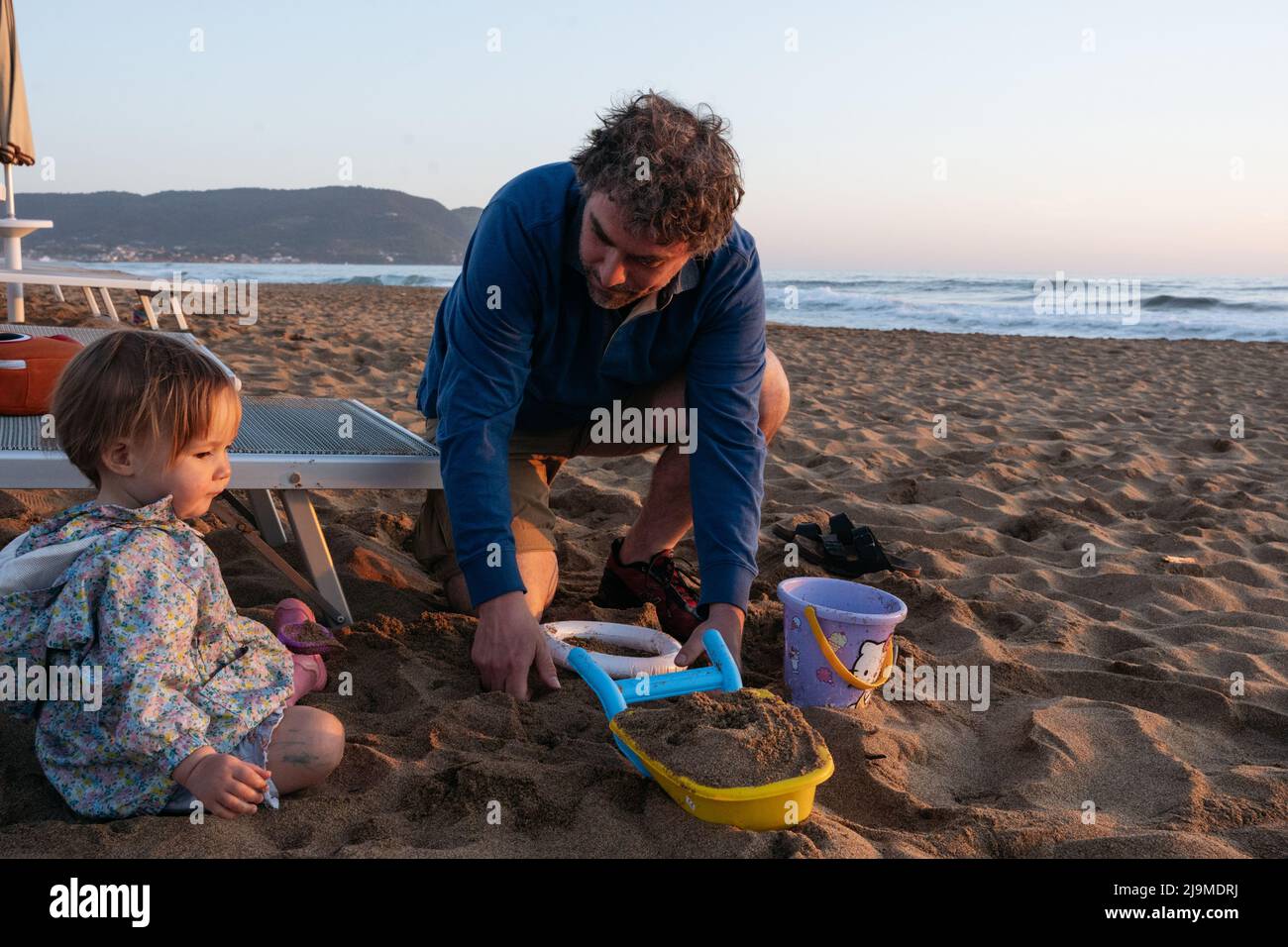 Padre y niño sentados en la playa al atardecer Foto de stock