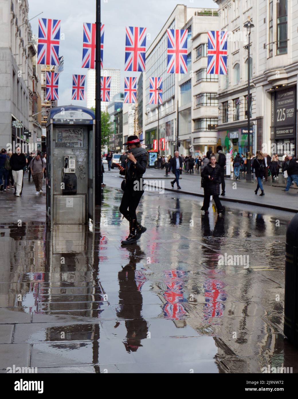 Londres, Gran Londres, Inglaterra, 11 2022 de mayo: Peatones en Oxford Street después de fuertes precipitaciones con Union Jacks reflejadas en el agua. Foto de stock