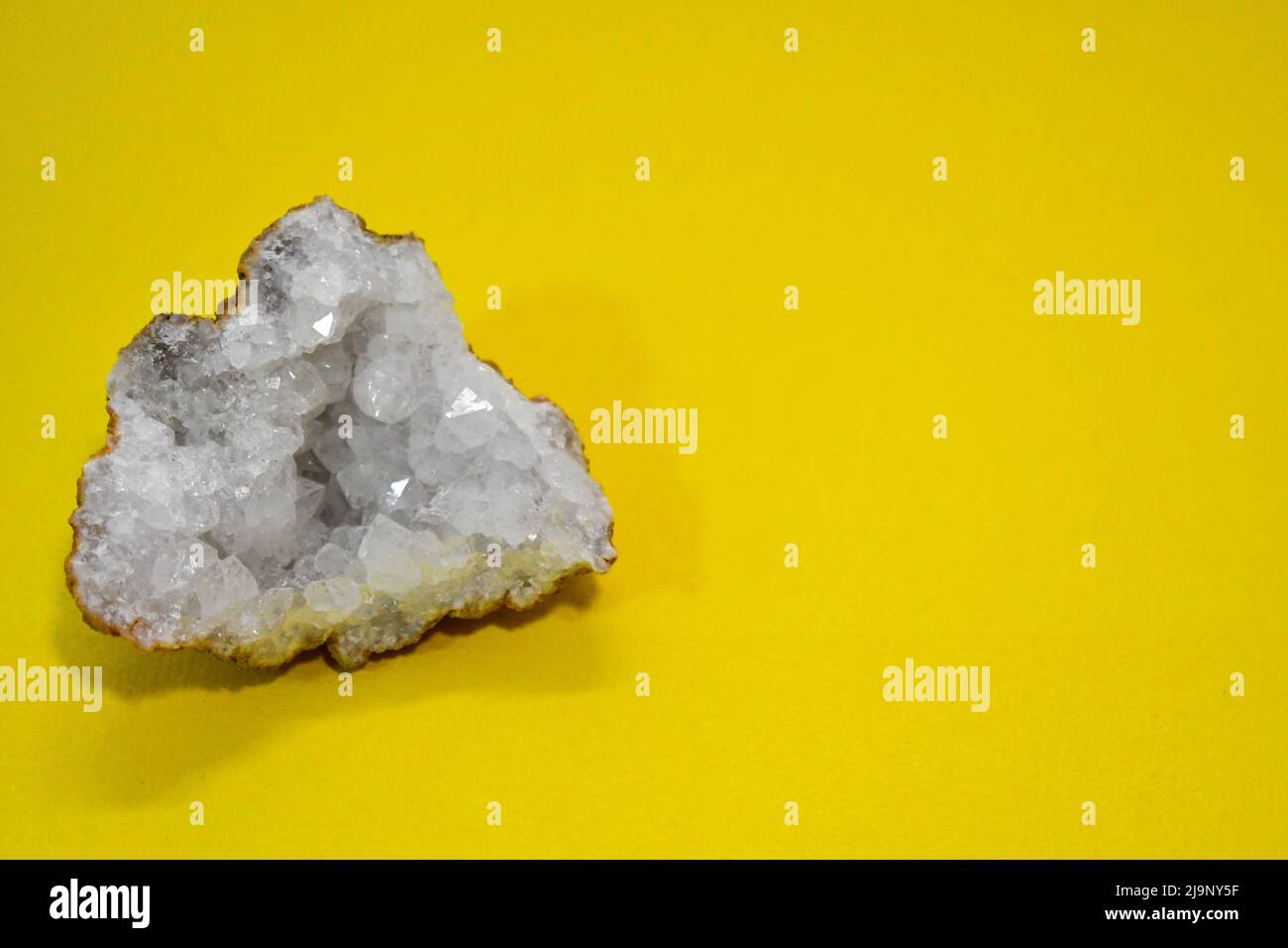Hermosa geoda de cuarzo de cristal transparente sobre fondo amarillo Foto de stock