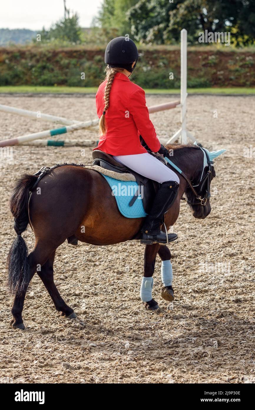 Chica de ropa roja montando en poni sobre pequeños saltos. Foto de stock